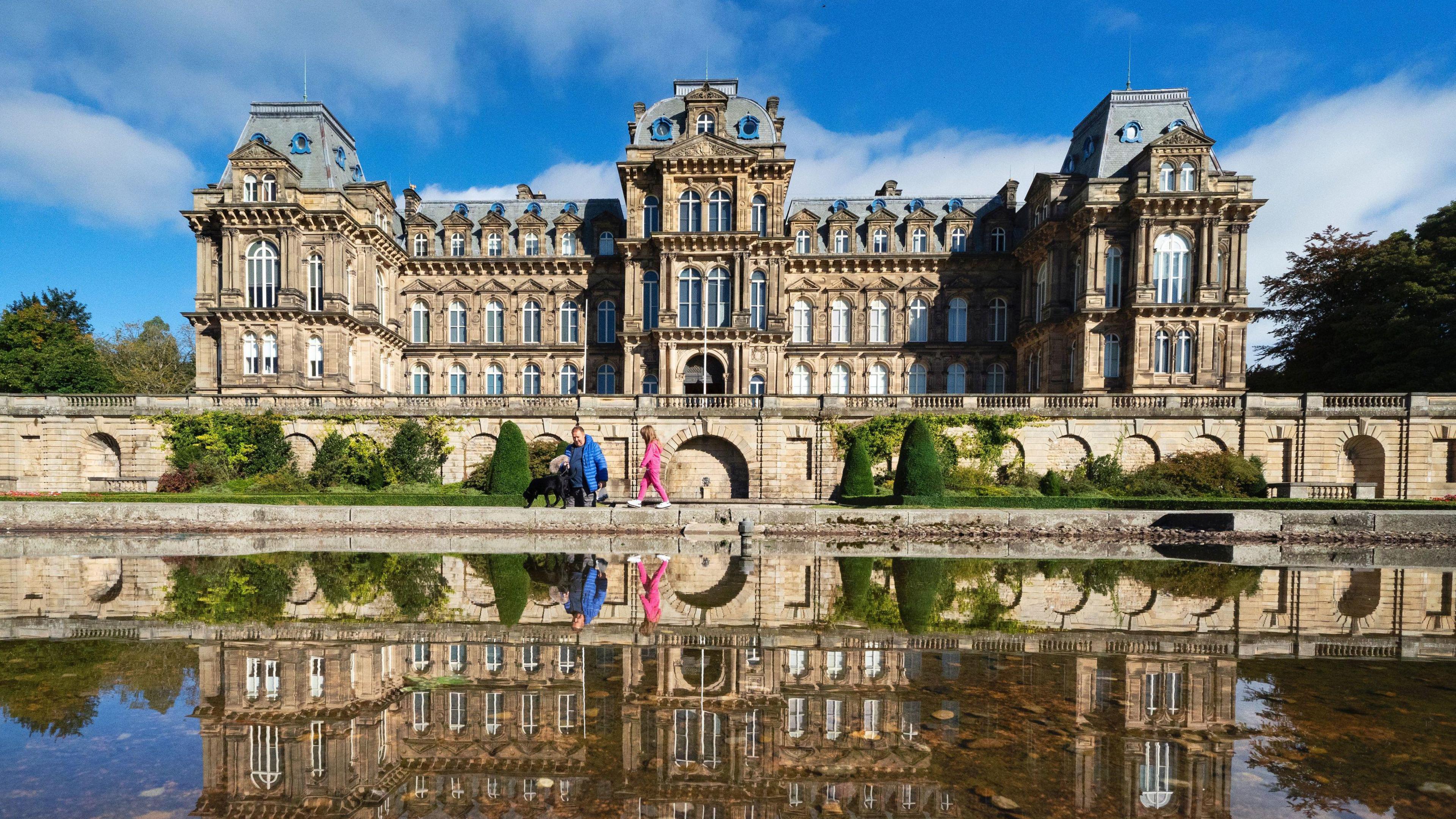 A man with his granddaughter and dog in front of the Bowes Museum in County Durham.