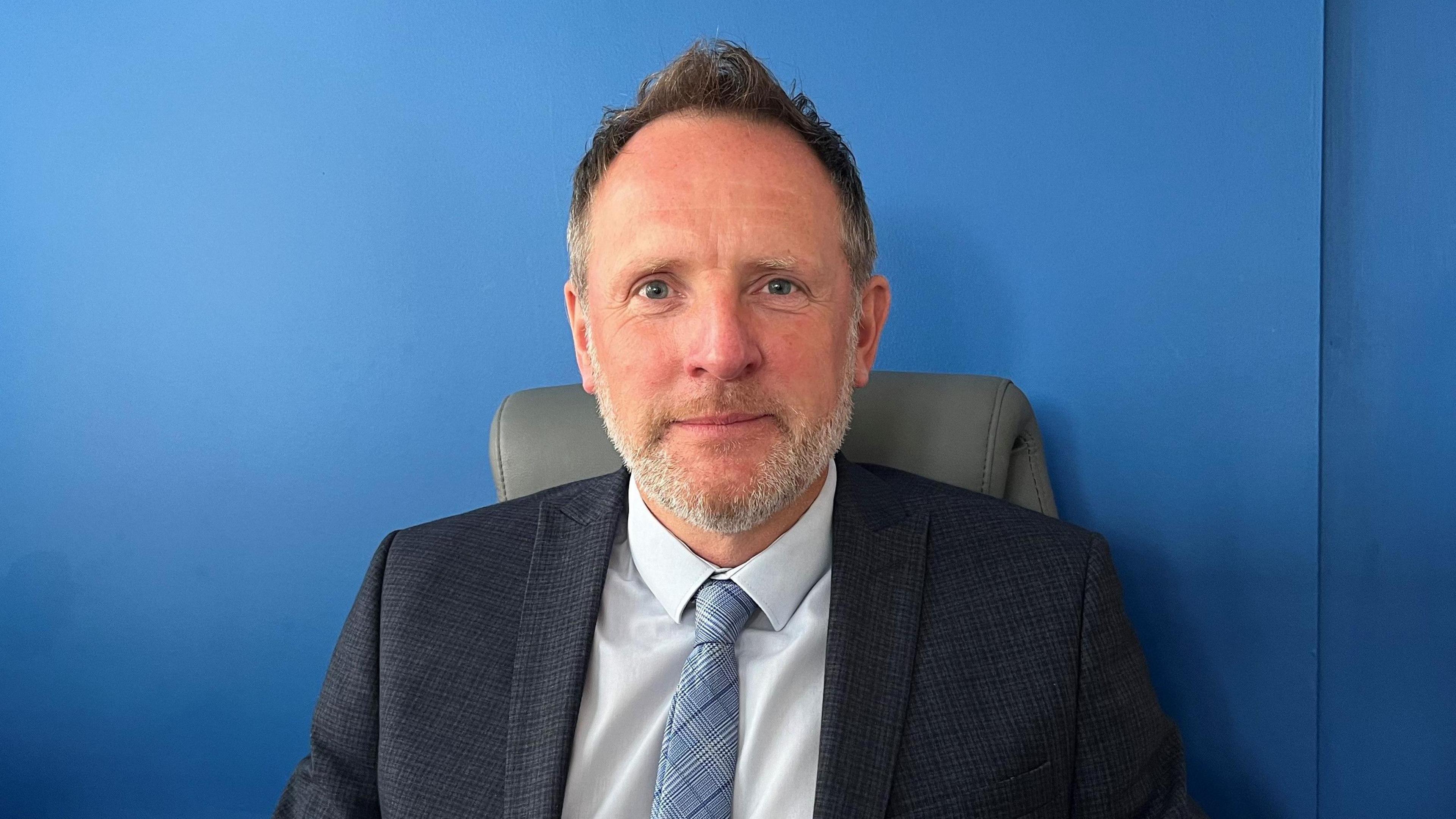 Portrait image of David Turner, a white man with a grey beard wearing a suit and tie