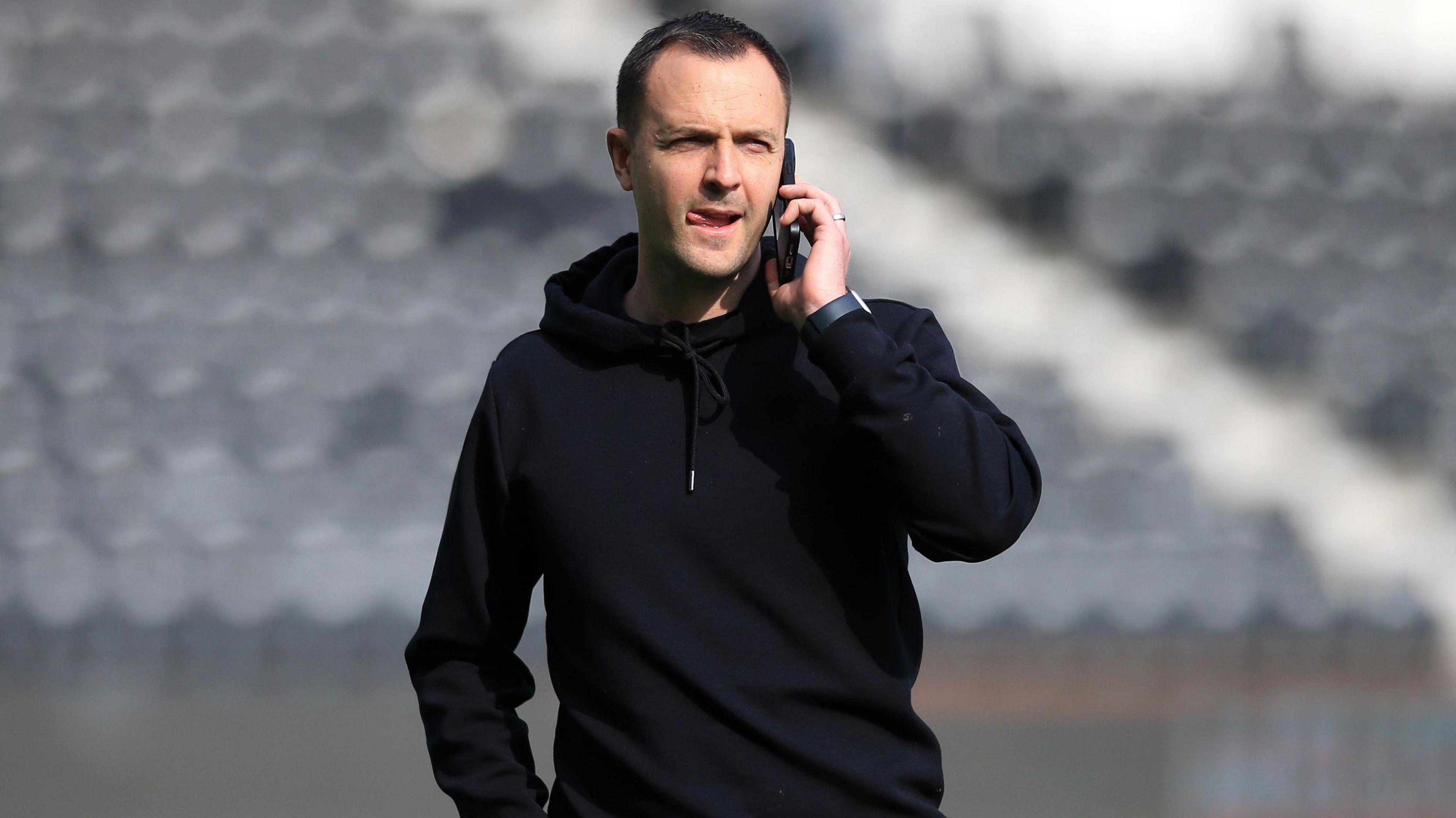 Chris Davies, pictured inside an empty stadium, talking on the phone