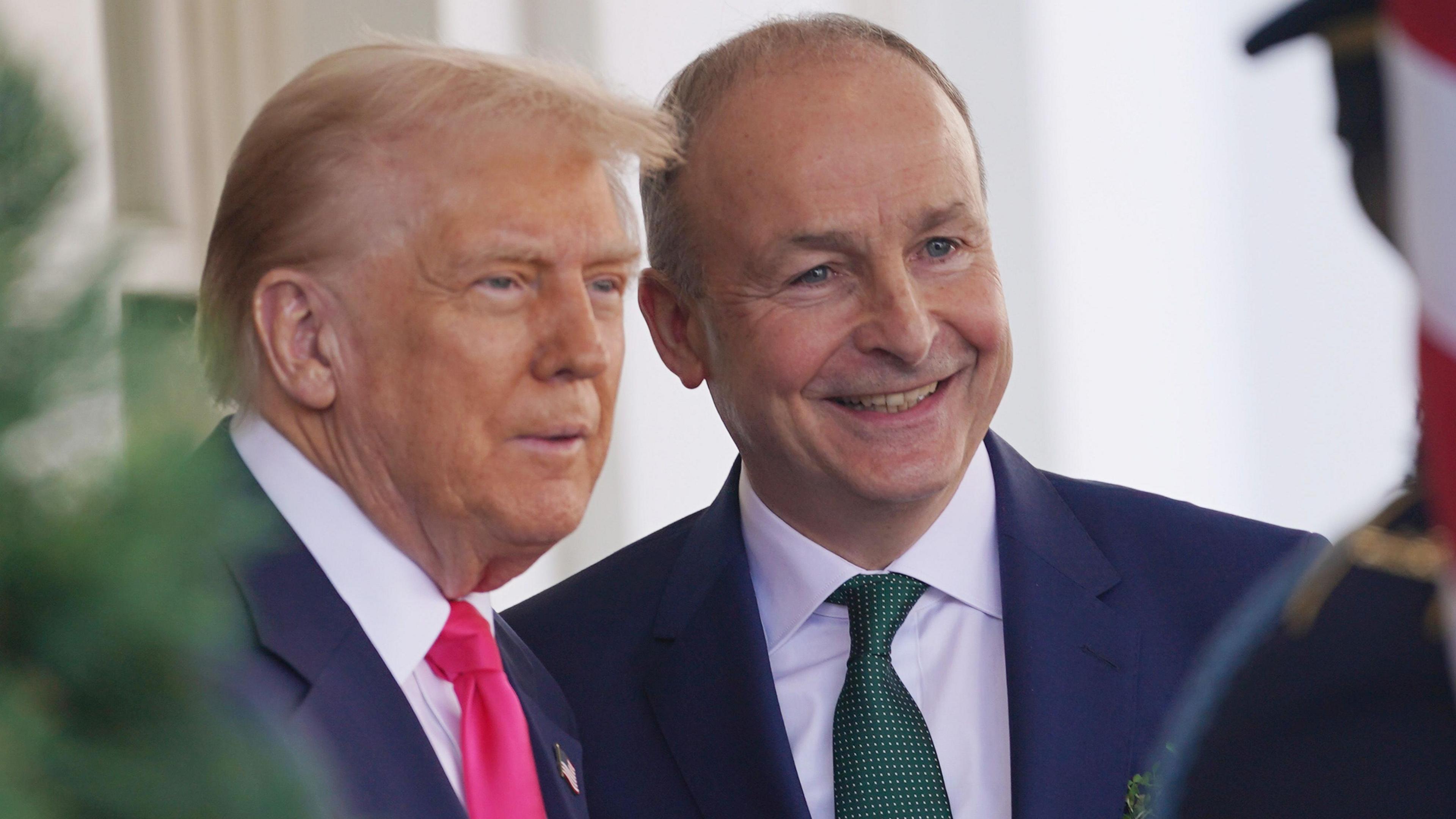 Donald Trump and Micheál Martin standing next to each other. Both men are wearing suits. Donald Tump has a red tie and Micheál Martin a green one