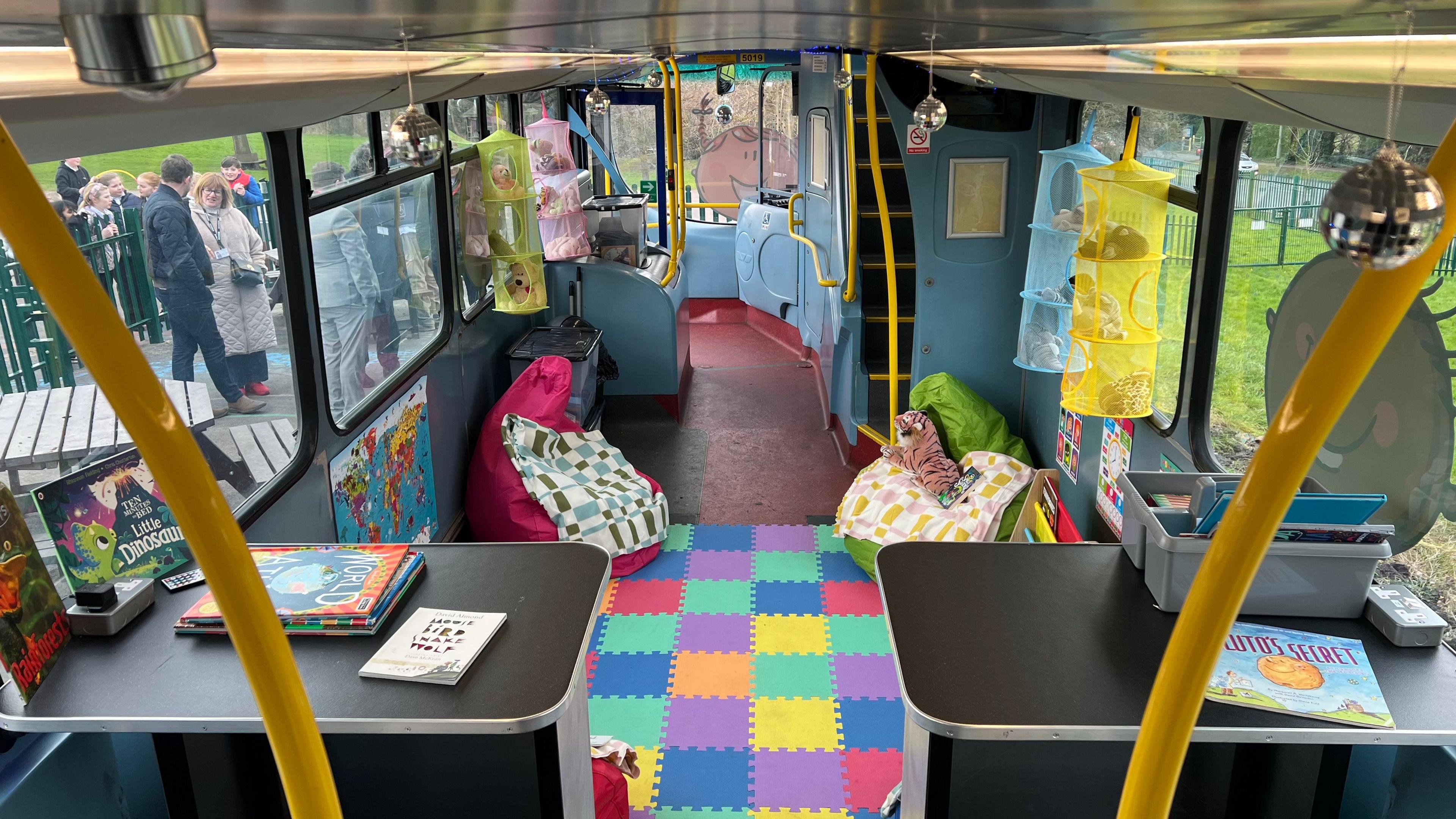 A view of the lower deck of the bus that has been transformed it o a play and reading area with a soft play floor and beanbags