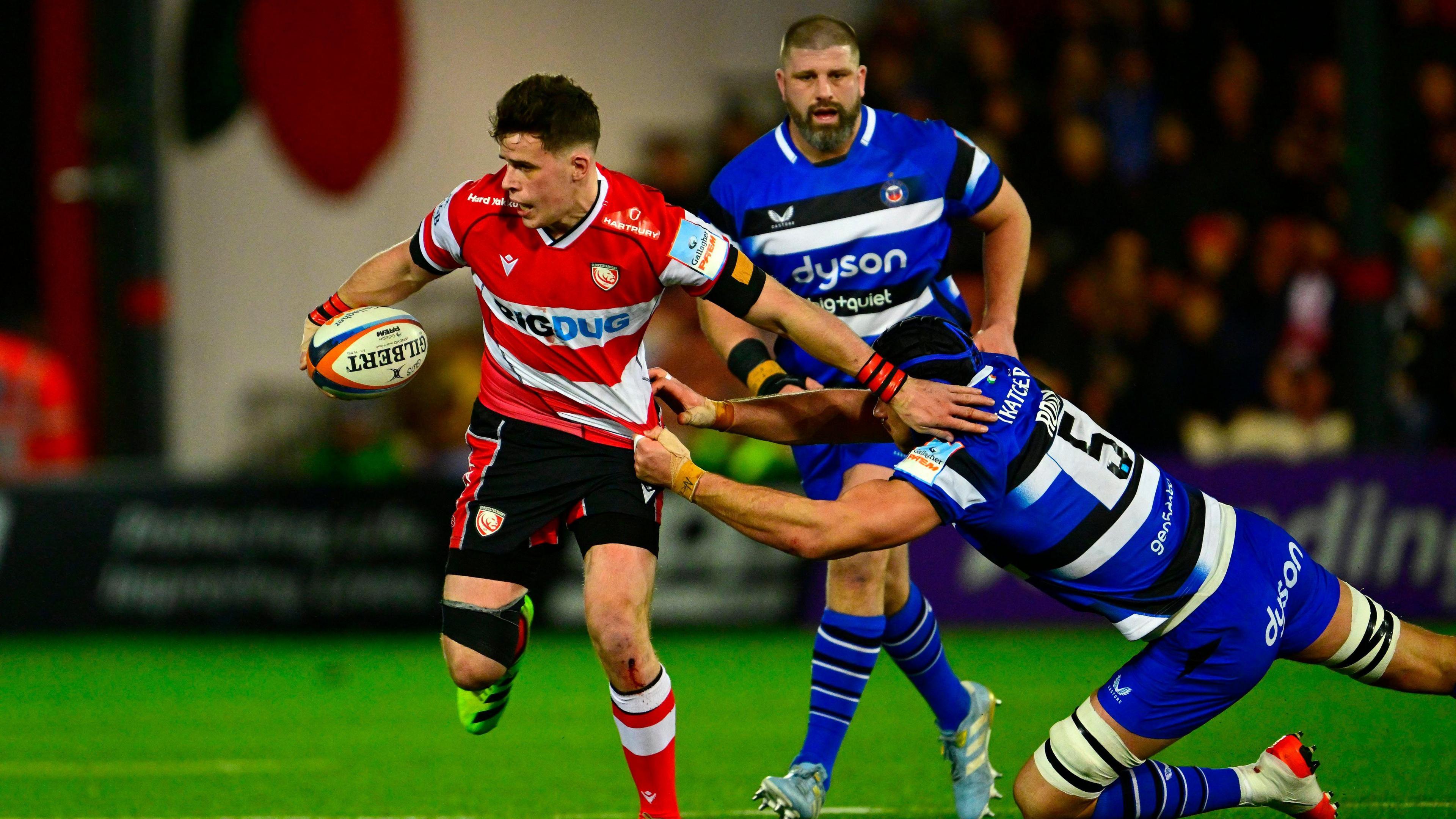 Seb Atkinson holds the ball in one hand and stretches the other out to fend off a tackle while Bath's Quinn Roux holds onto his jersey with two hands 