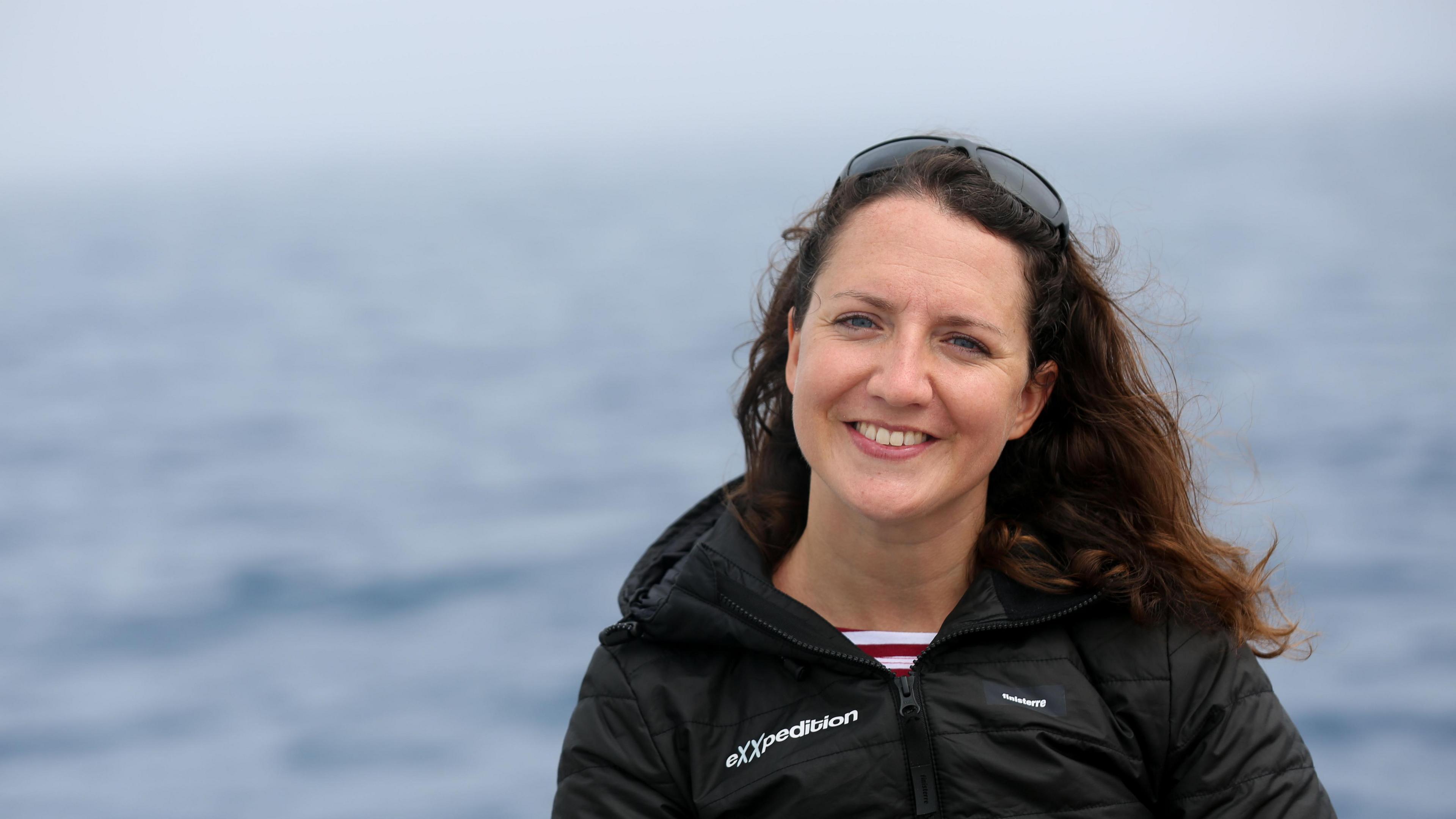 Sally Earthrowl wearing a black jacket in front of a background of the sea