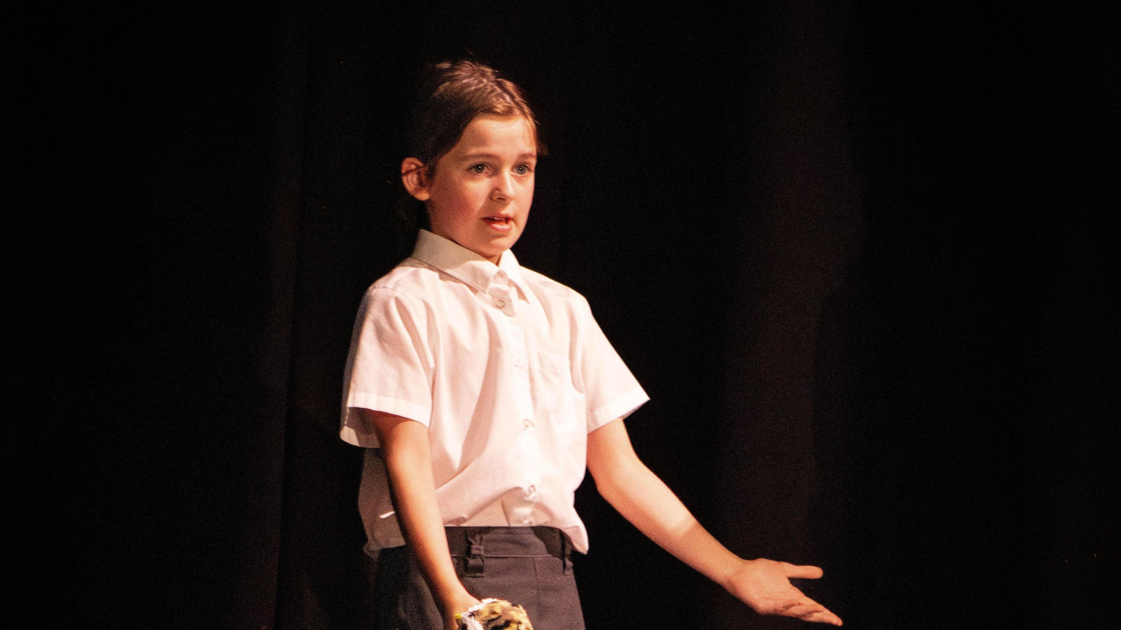 Evie on stage performing a song in a white shirt. The backdrop is pitch black 