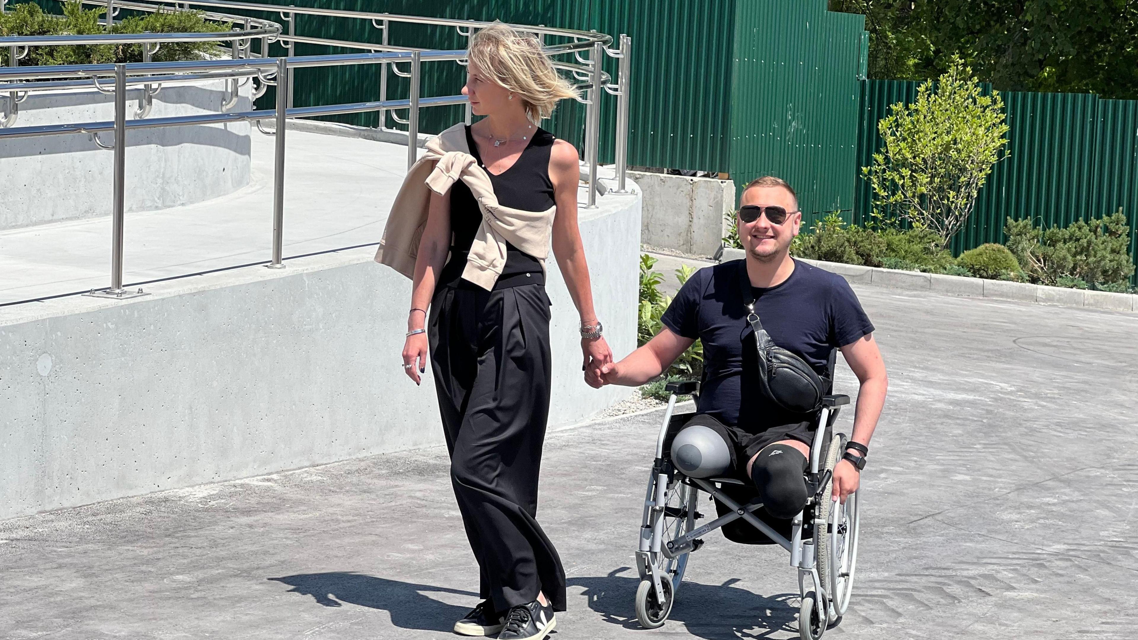 Olga Rudnieva walks next to a ramp holding the hand of one of the amputees in her trauma centre - a man with a double leg amputation in a wheelchair