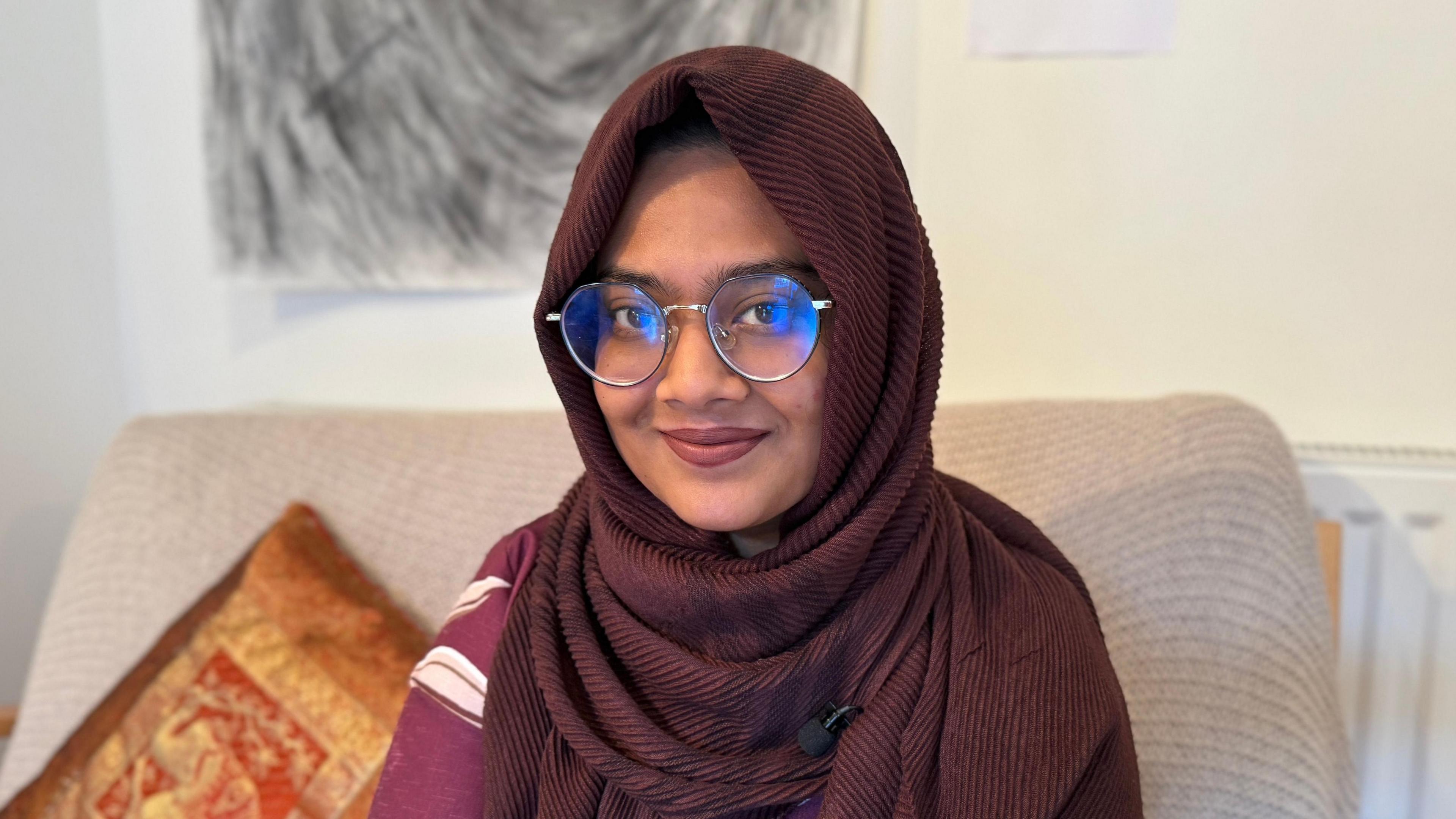 Nusaiba Maisha looks at the camera. She has large round glasses and is wearing a burgundy hijab covering her head and shoulders.