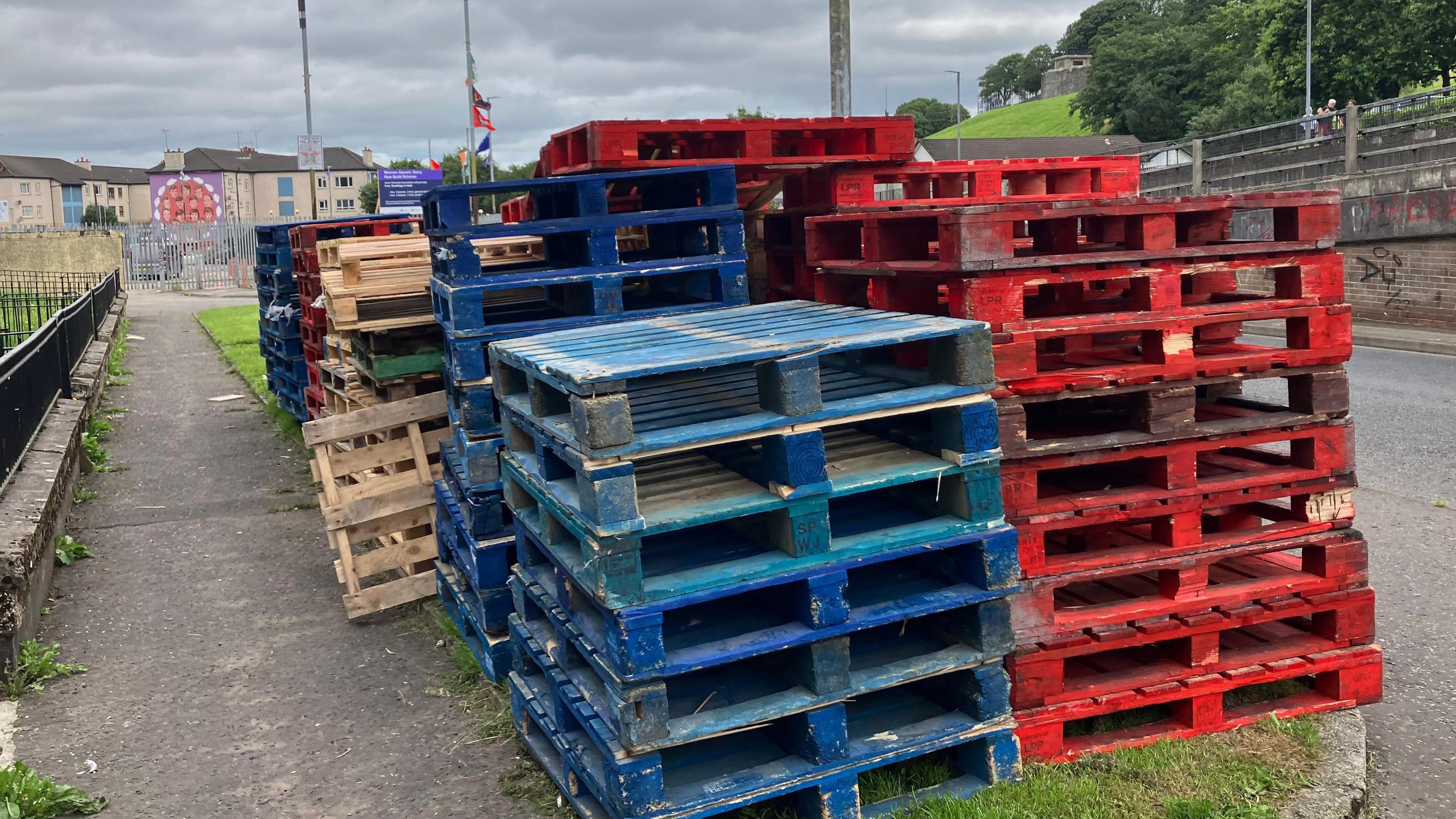A number of stacked wooden pallets sit on the side of a road