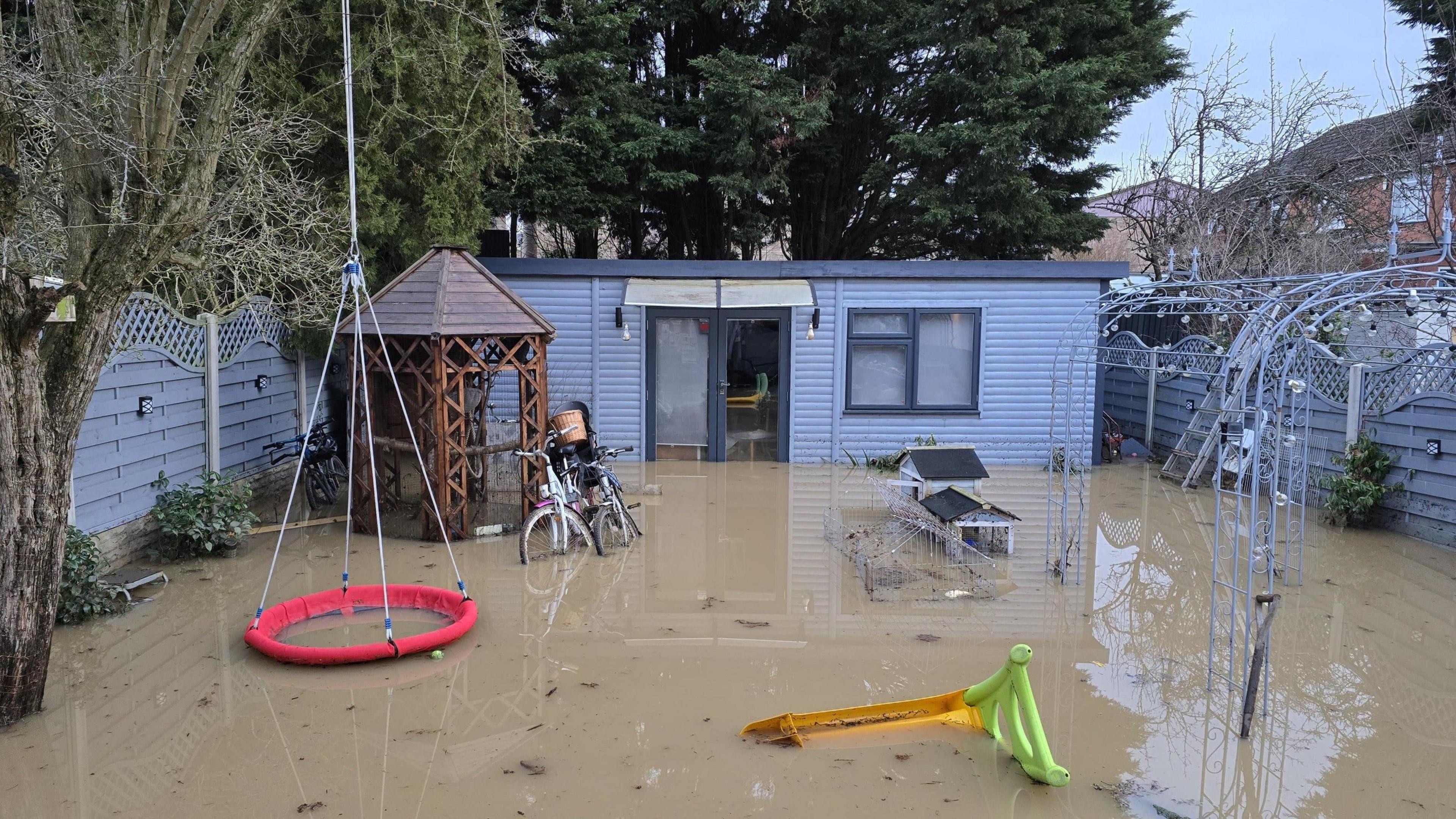 An out building in a back garden surrounding by flood water 