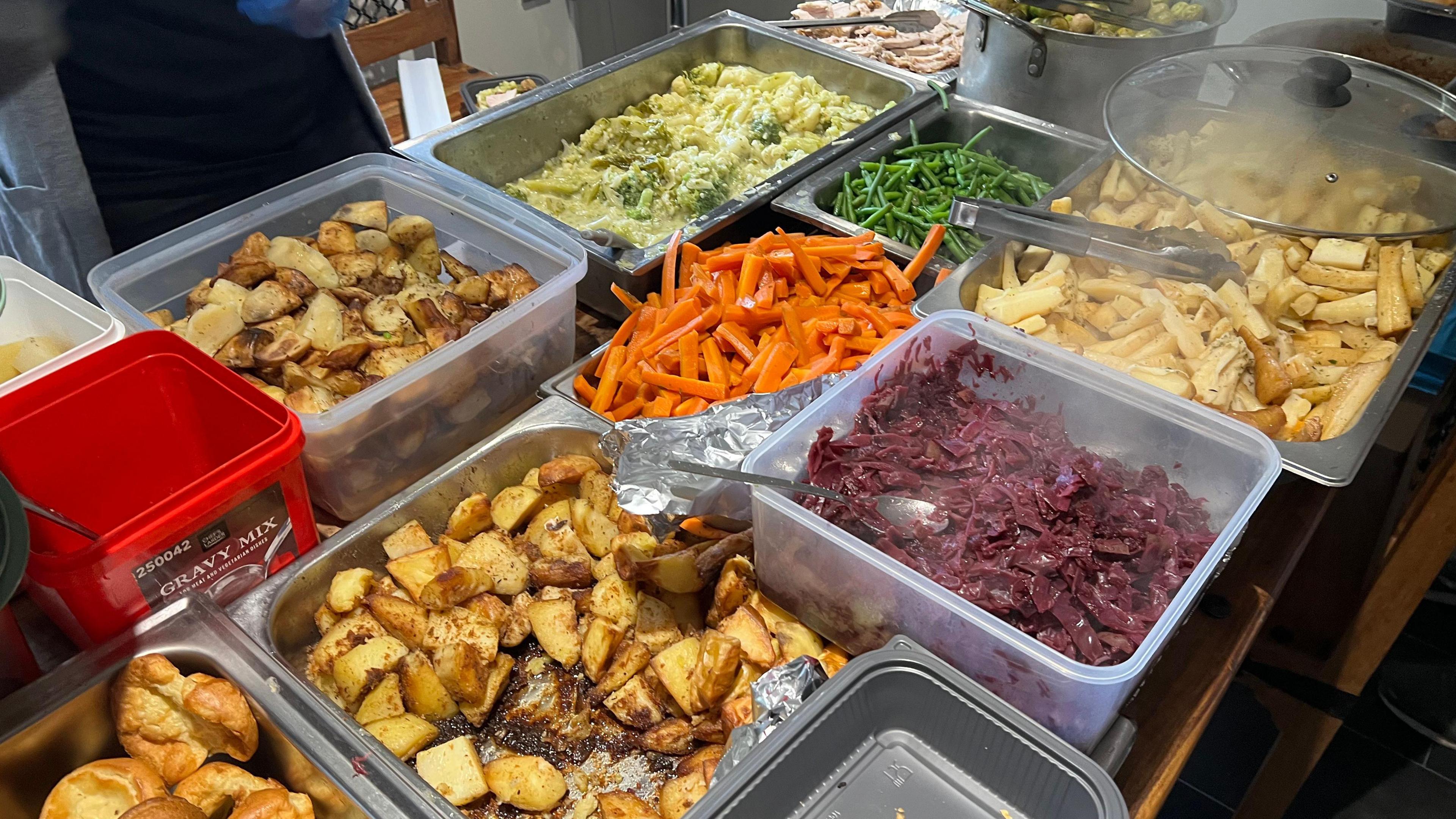 Metal containers are pictured on a table next to each other, full of carrots, red cabbage, roast potatoes, Yorkshire puddings, green beans, parsnips, cauliflower cheese, sprouts and turkey.