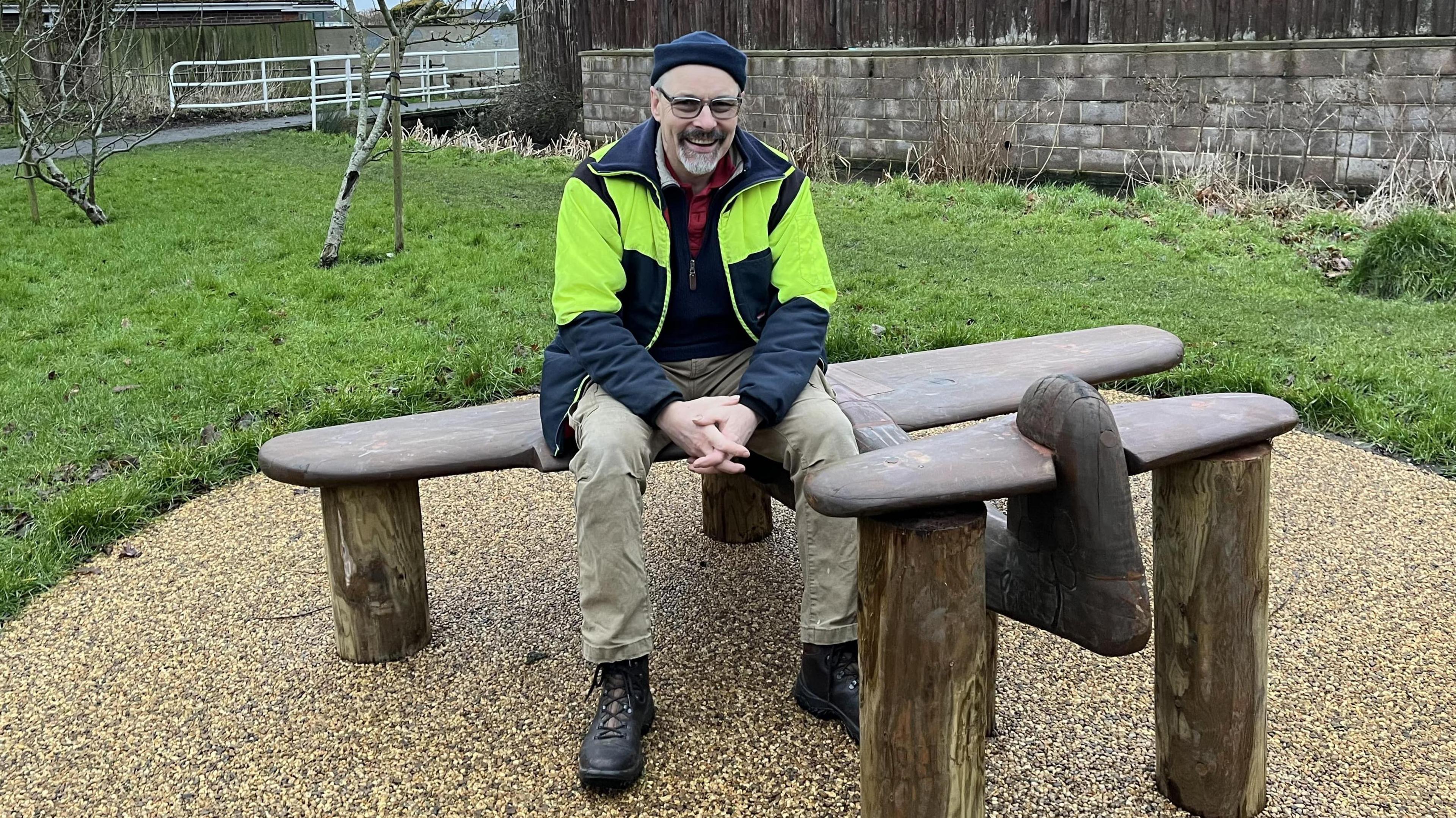 Kevin Prosser sat on the wooden aircraft bench. He is looking into the camera and smiling. 