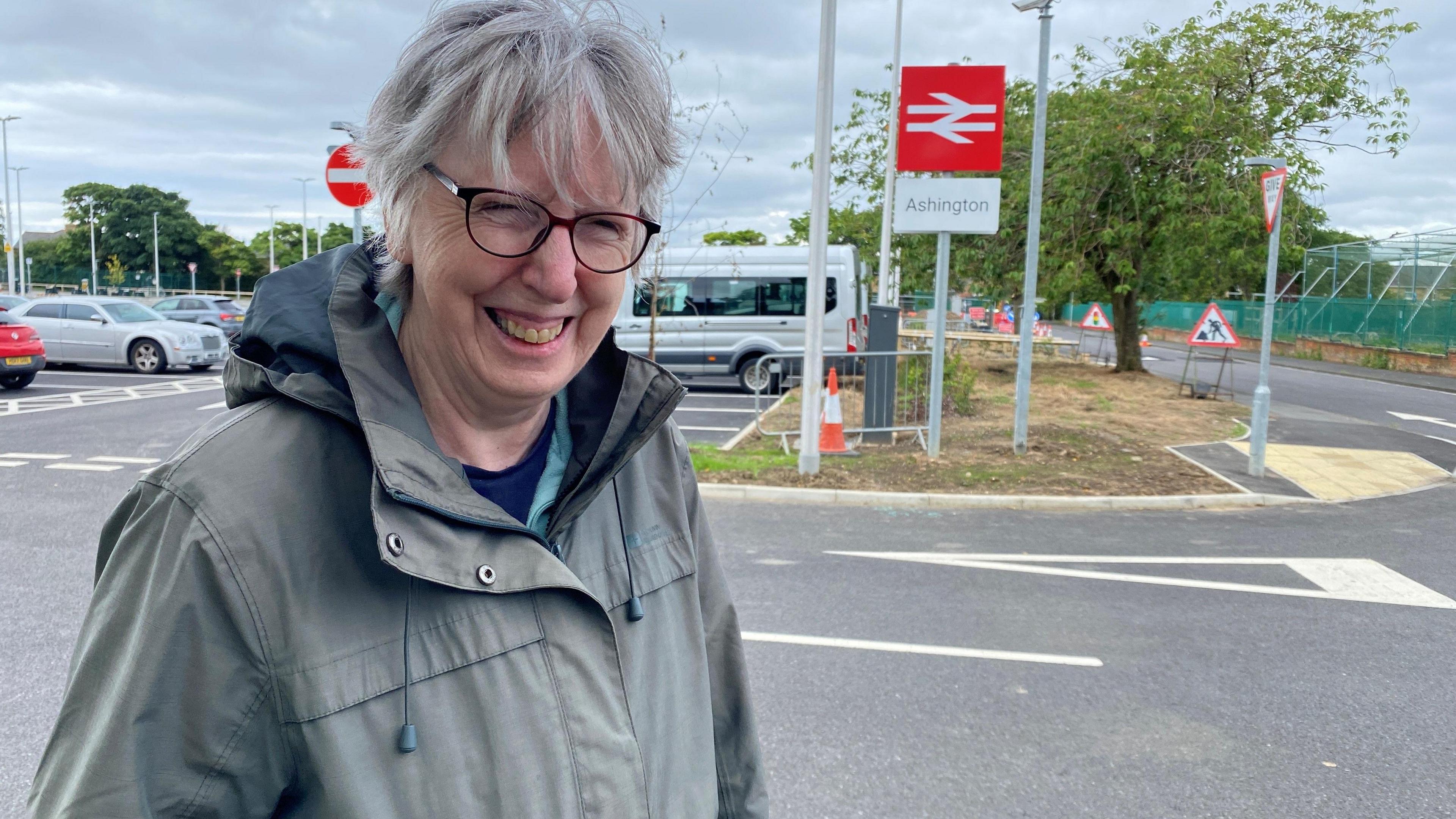 A woman standing in front of a sign to Ashington station 