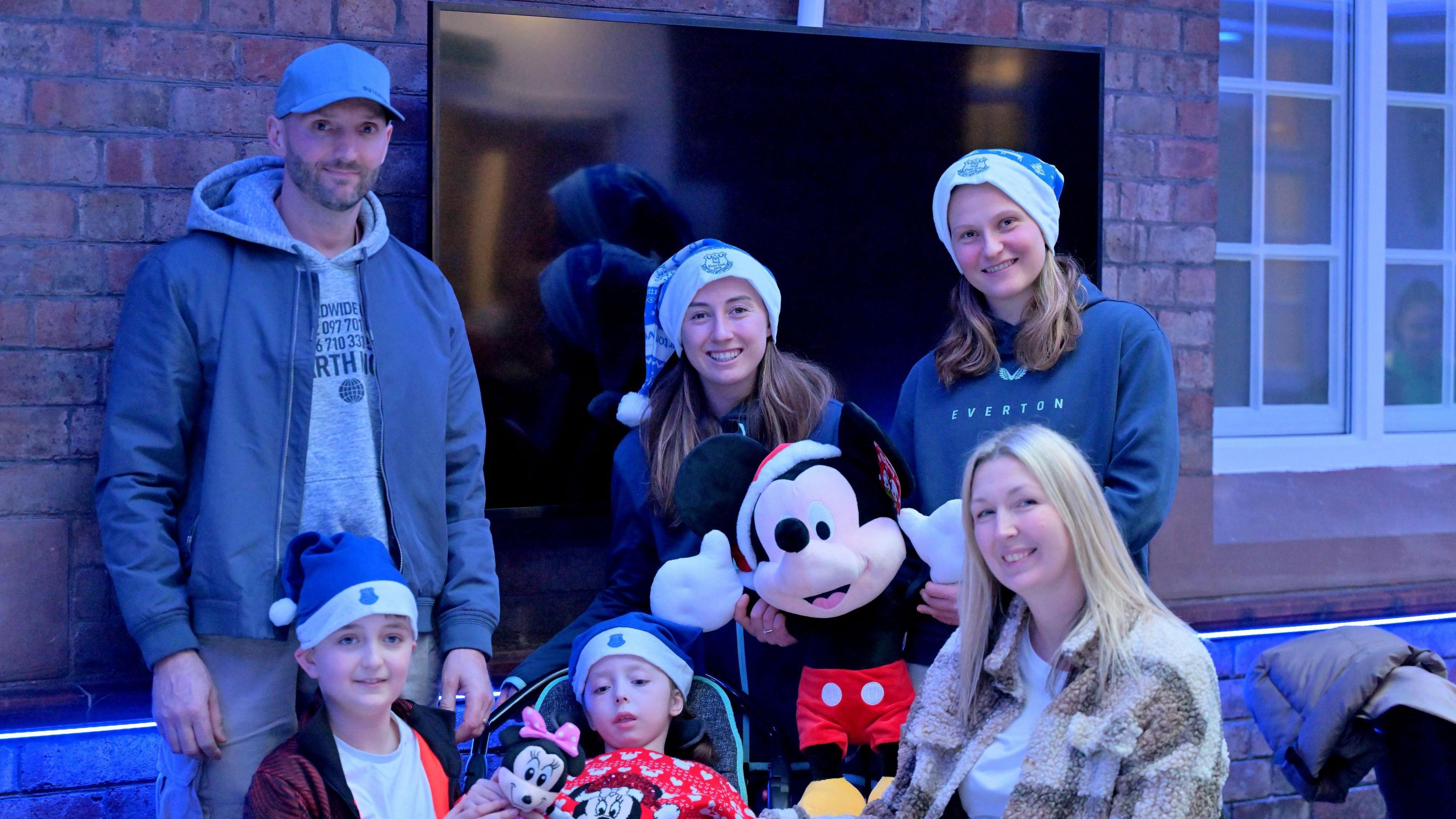 Elise Stenevik and Claire Wheeler smile at the camera with a father, mother and two children, holding Micky and Minnie Mouse toys 