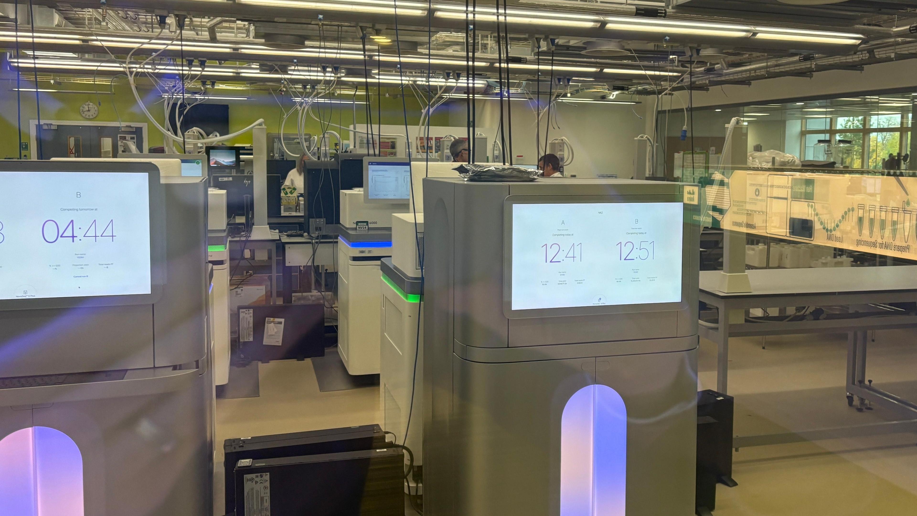White machines are dotted around a room and have screens on the front which are displaying numbers. There are wires coming out from the top of the machines. 