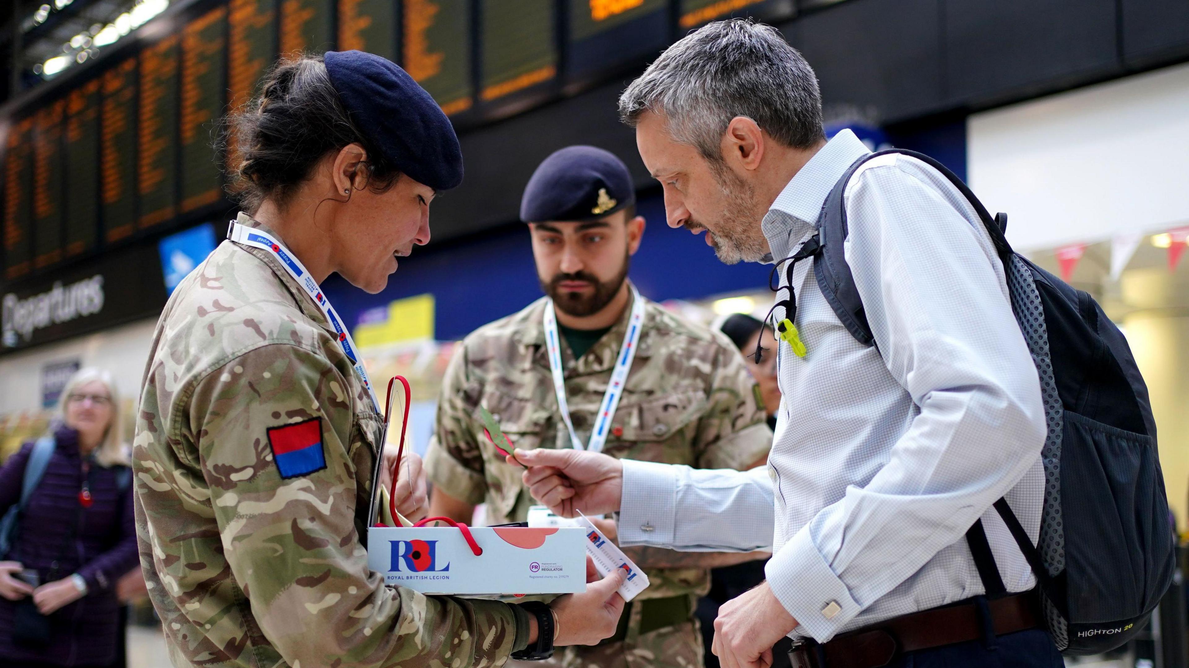 A man wearing a white shirt is buying a poppy from a female member of the military. She is wearing a blue beret and combat uniform.