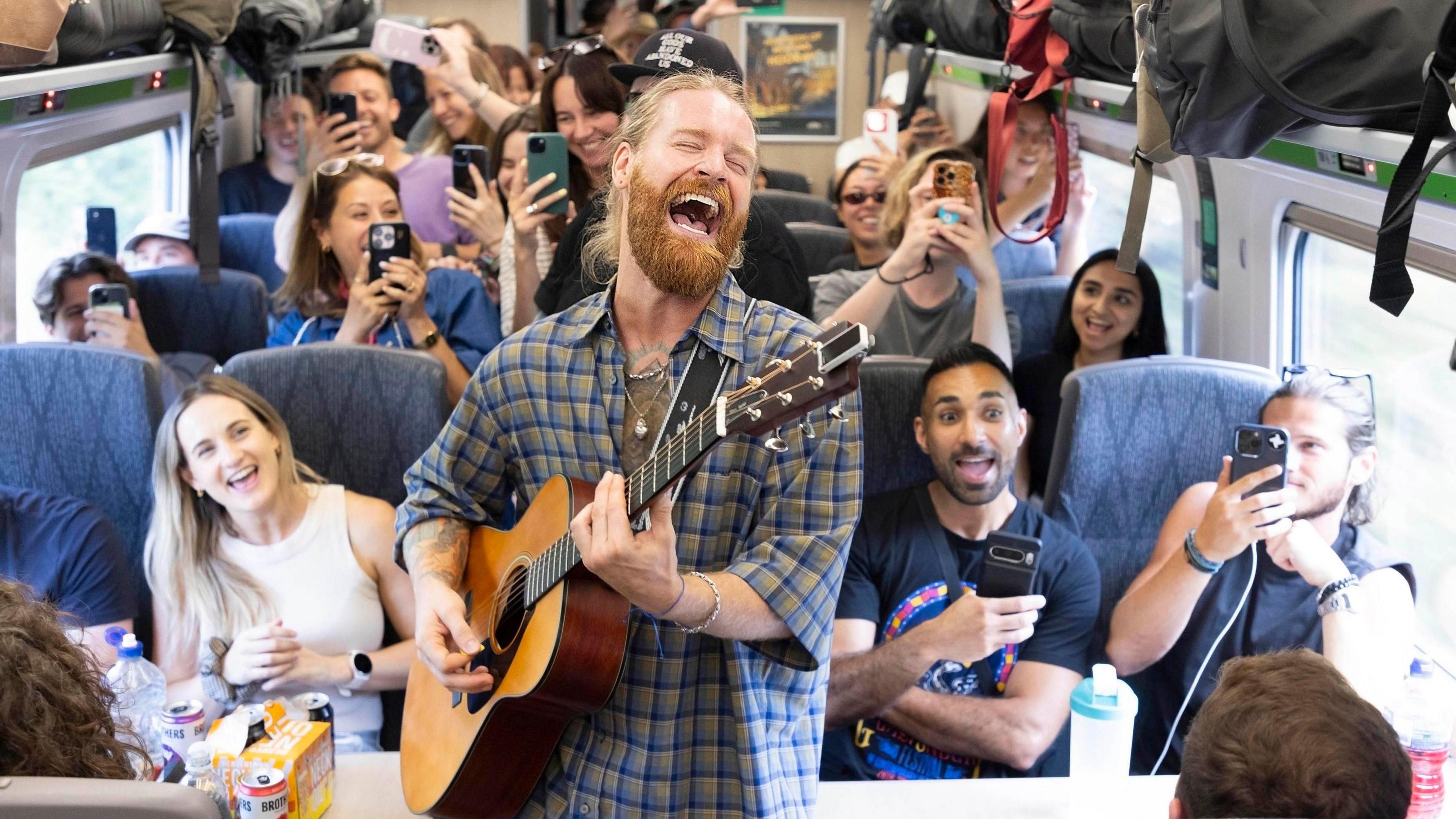 Sam Ryder - a bearded man with an acoustic guitar - singing in a packed train carriage