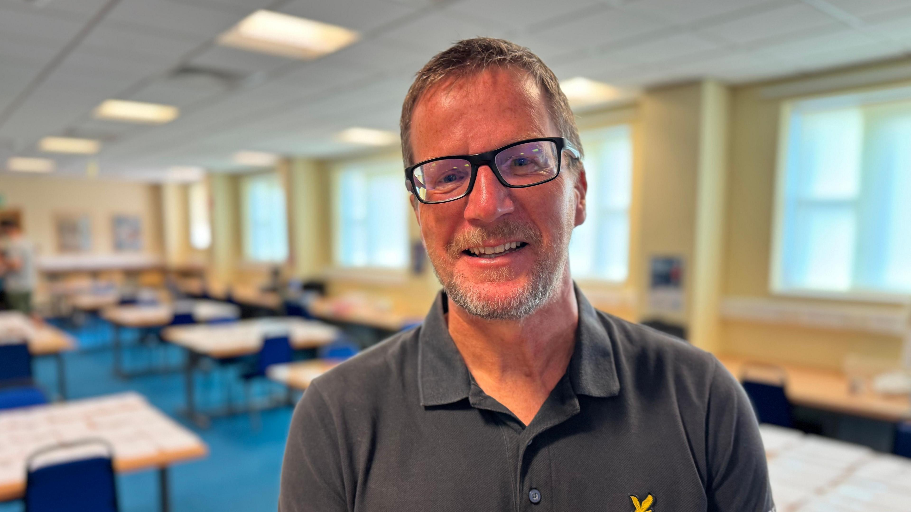 Graeme Corrin wears a blue polo neck and dark glasses. He has short greying hair and a beard.
