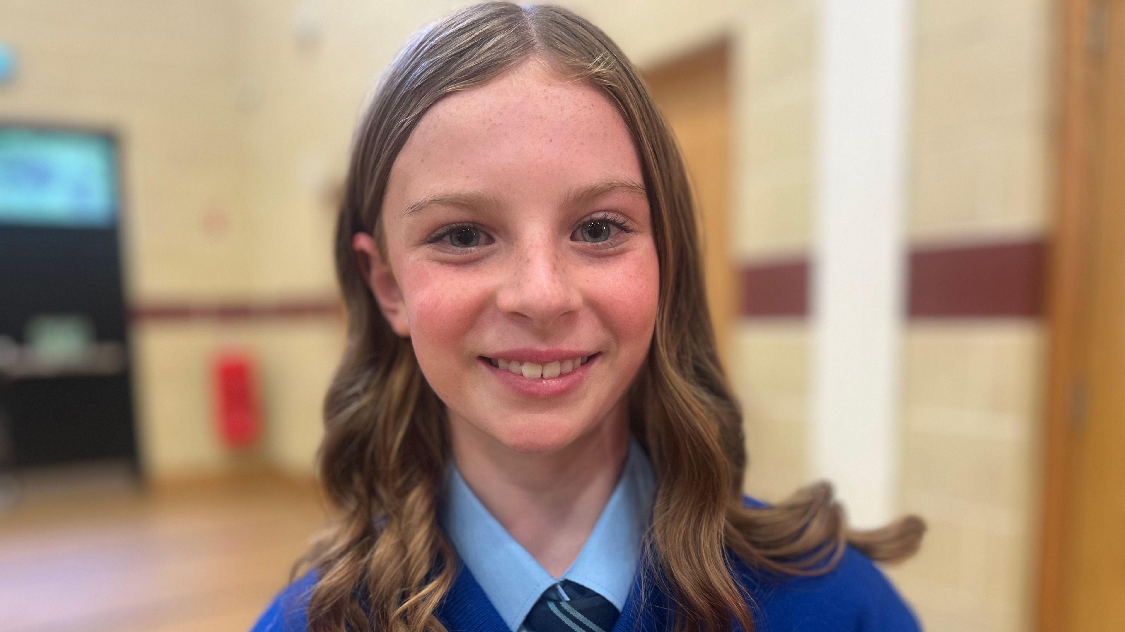 Caoimhe is smiling. Her hair is styled in curls. She's wearing a blue uniform.