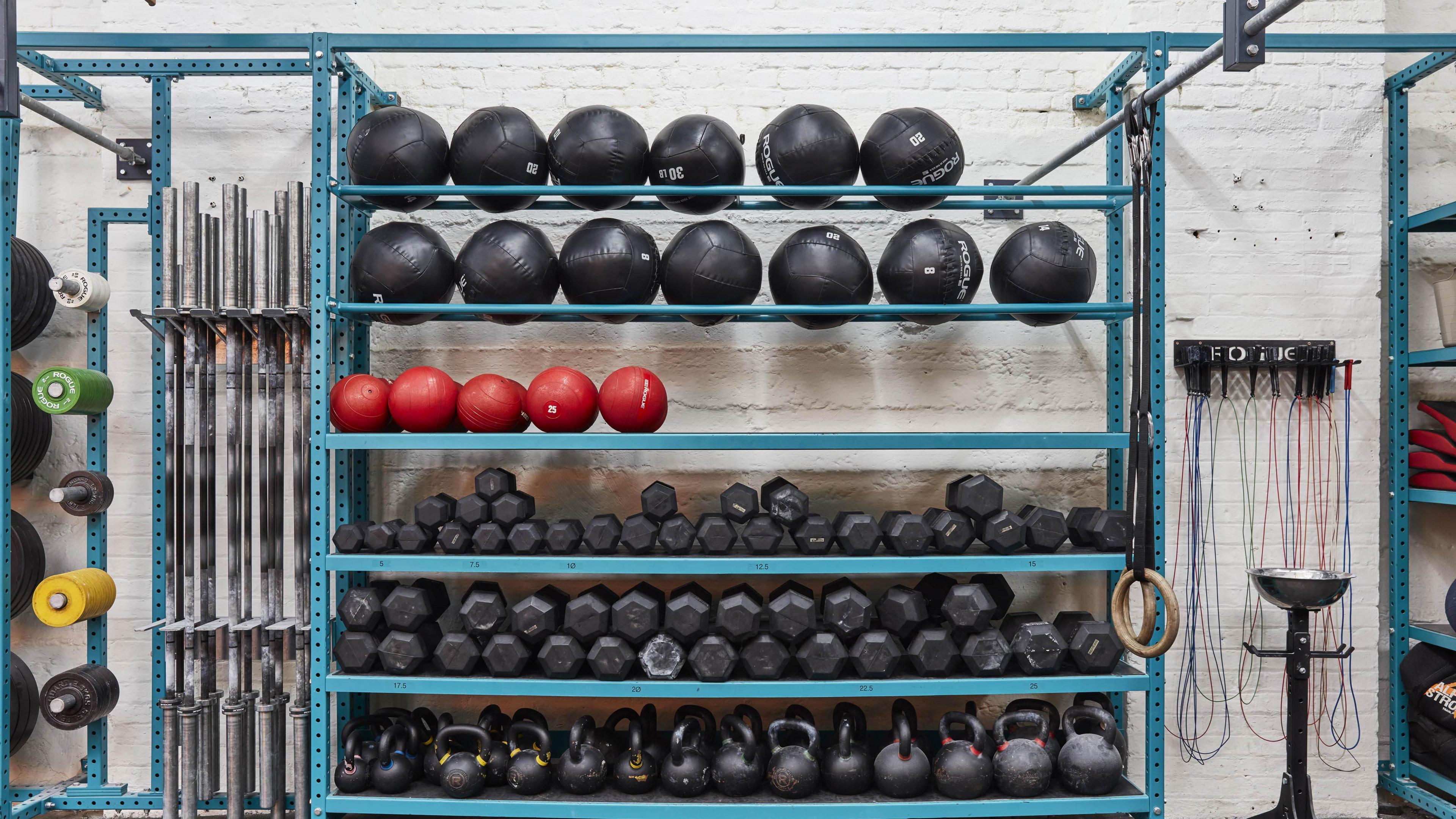 A set of medicine balls and weights placed on a blue shelf, against a white wall.