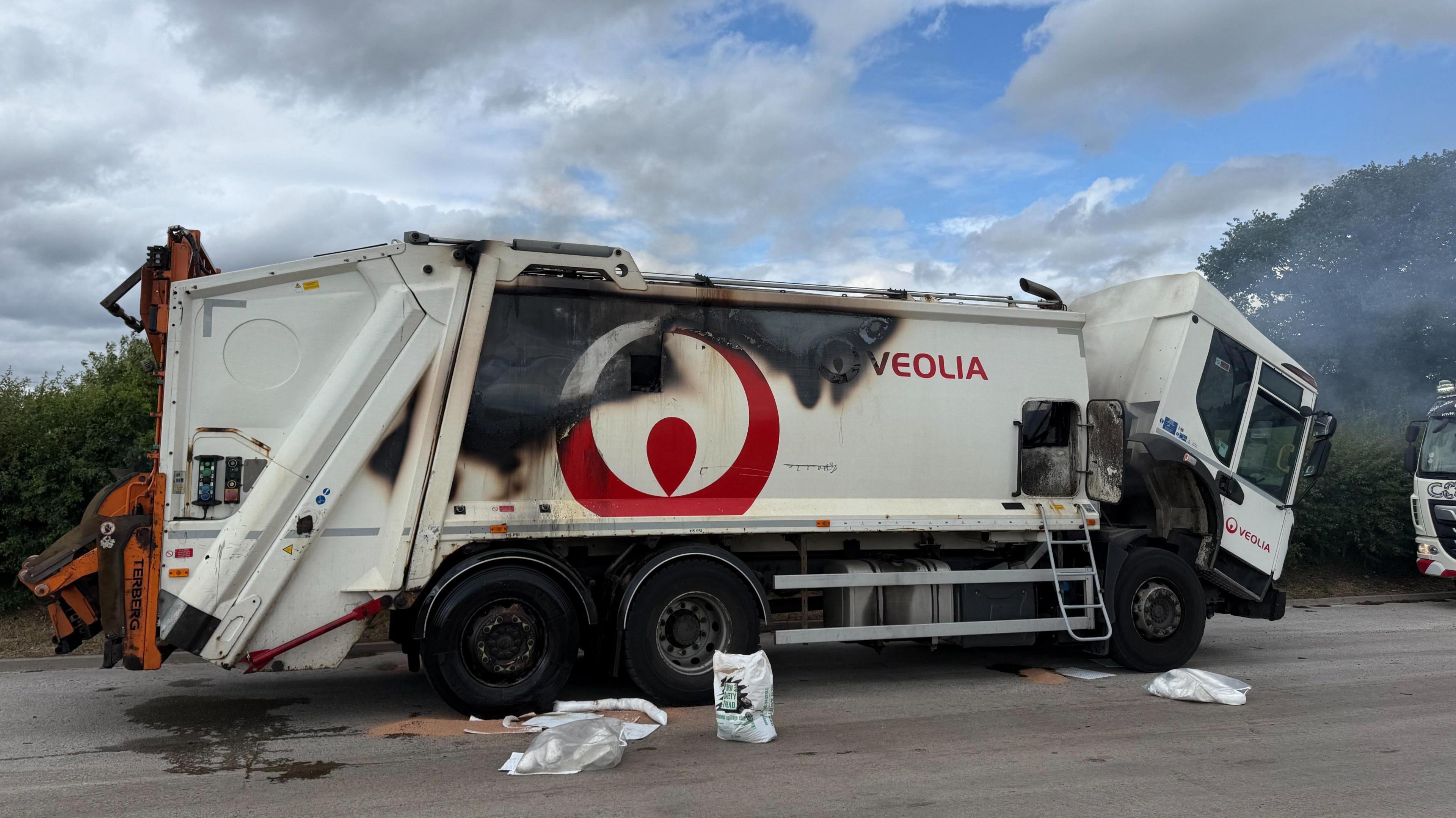 A white bin lorry stationary in the road, with clear scorch marks down the side