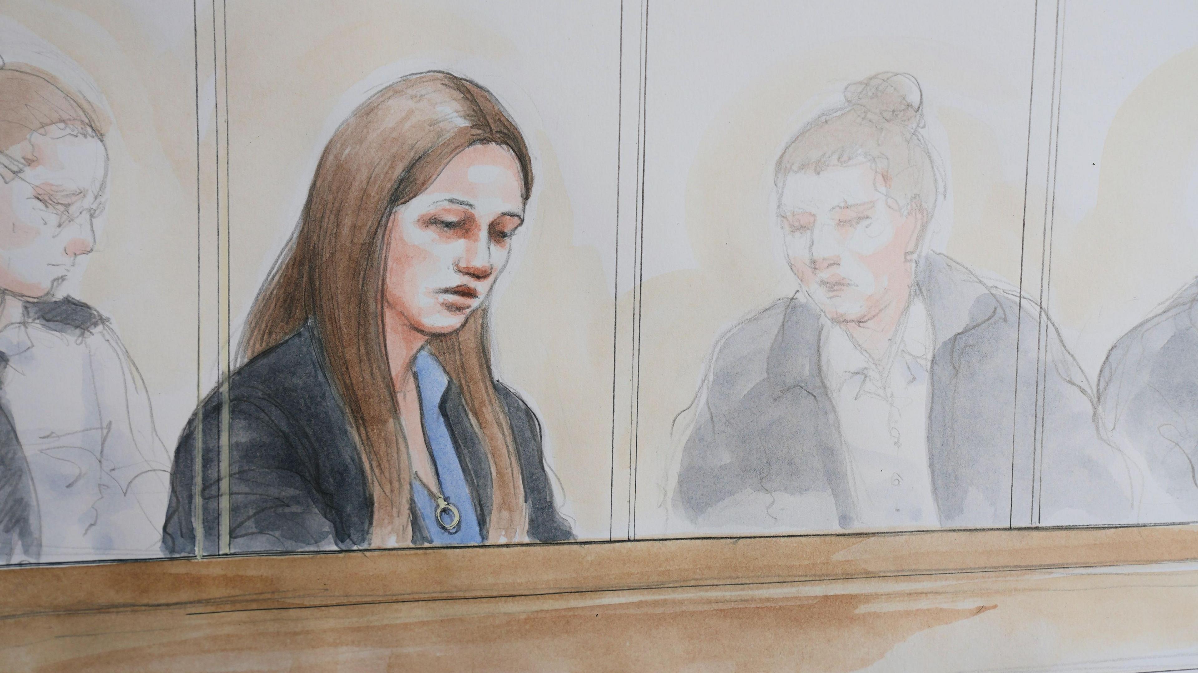 An artist impression/court drawing of Lucy Letby in the courtroom dock, she looks down and is wearing a black jacket and blue shirt, her hair is down and is long and brown. 