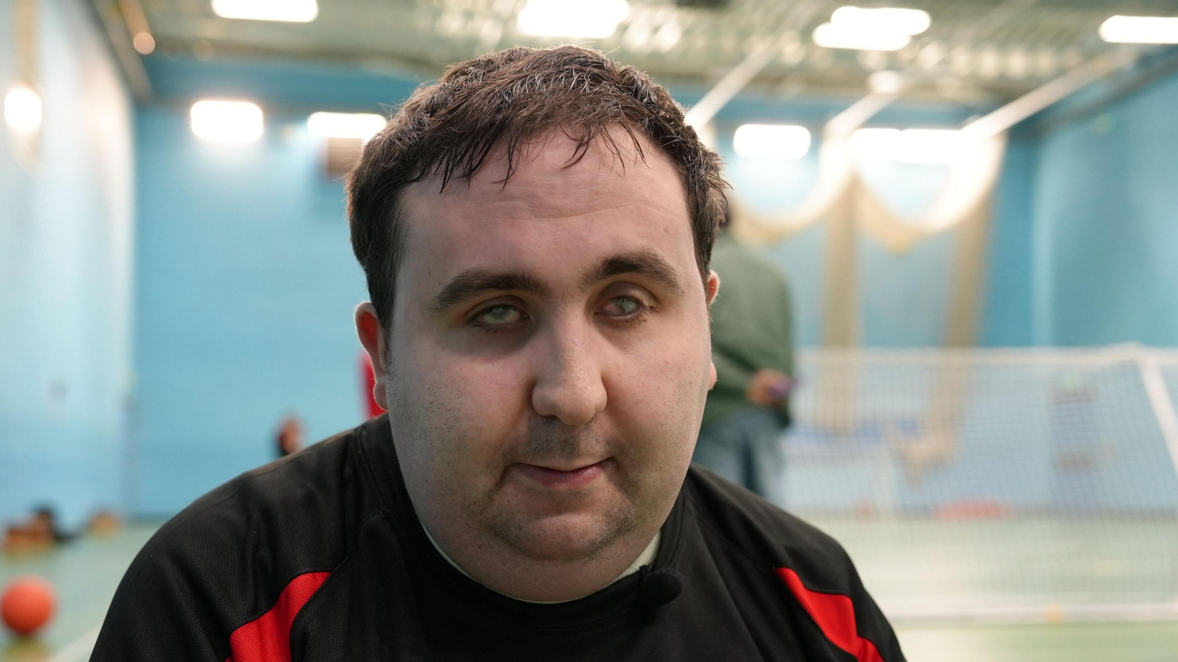 George Sullivan wearing a black and red top. He is sitting in a sports hall.