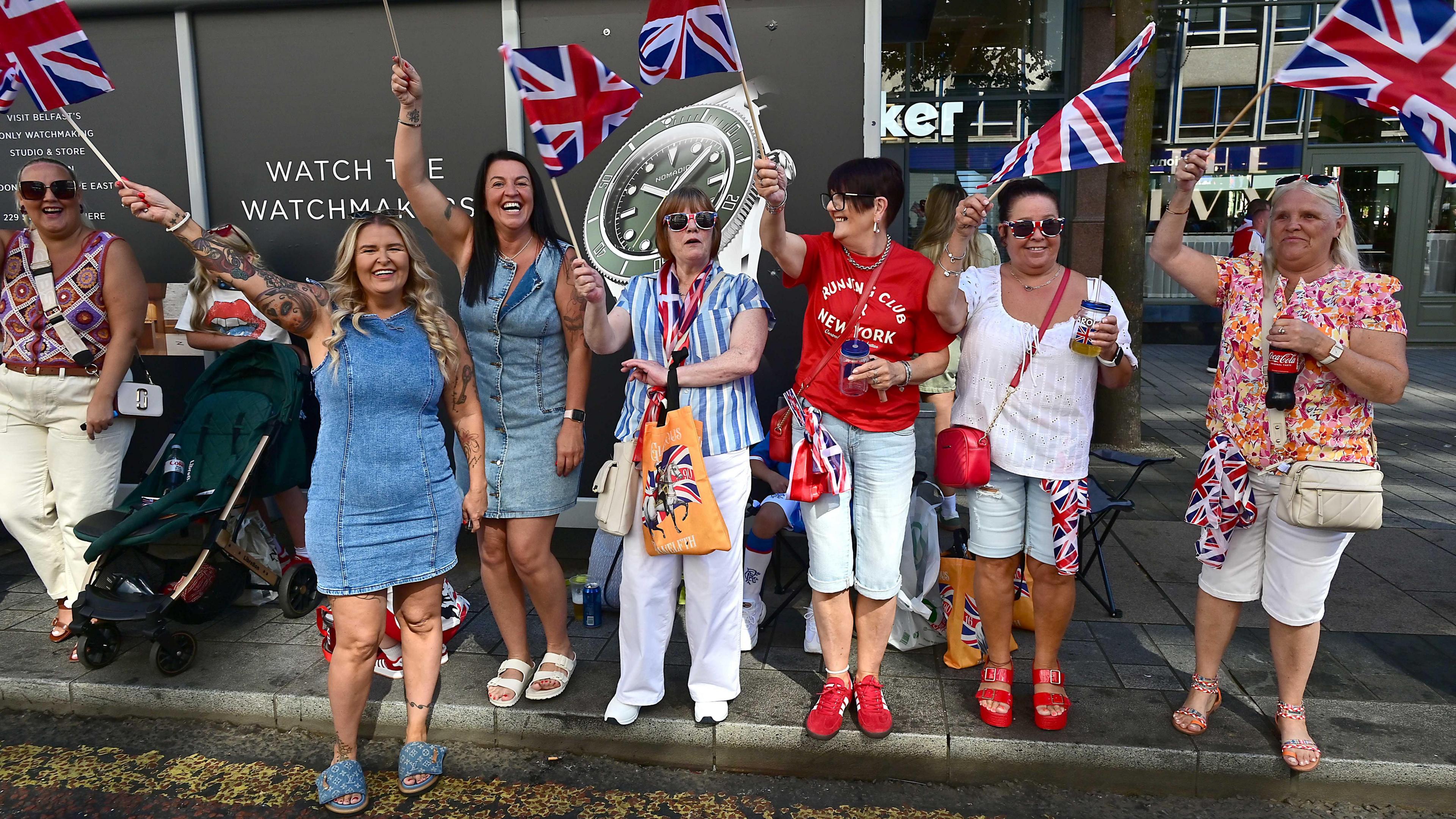 A group of women waving Union flags. They are dressed in red white and blue. 