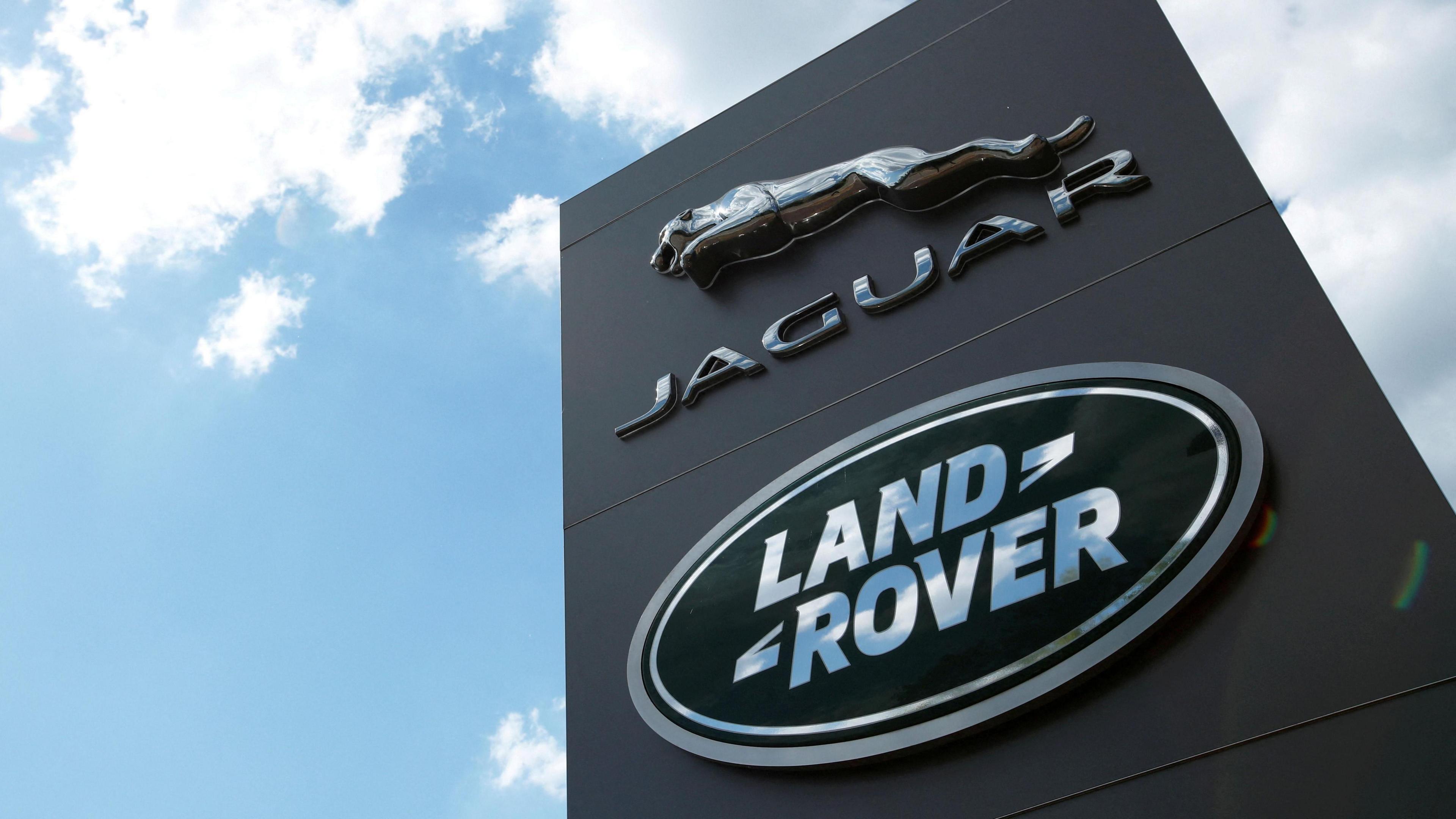 A shot looking up at a black sign with the Jaguar and Land Rover logos on, set against a blue sky with clouds.