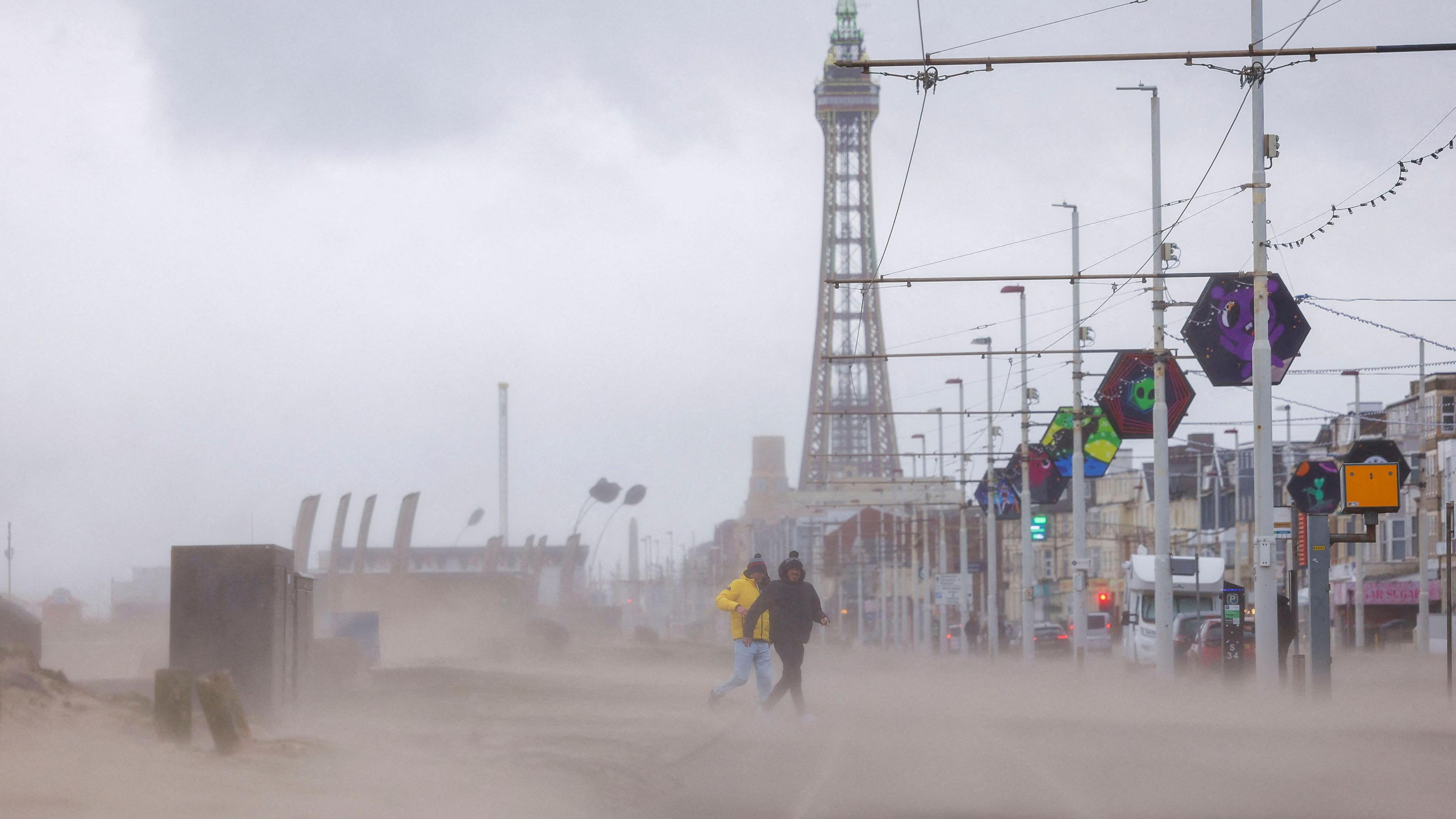 People run through wind and rain in front of The Blackpool Tower