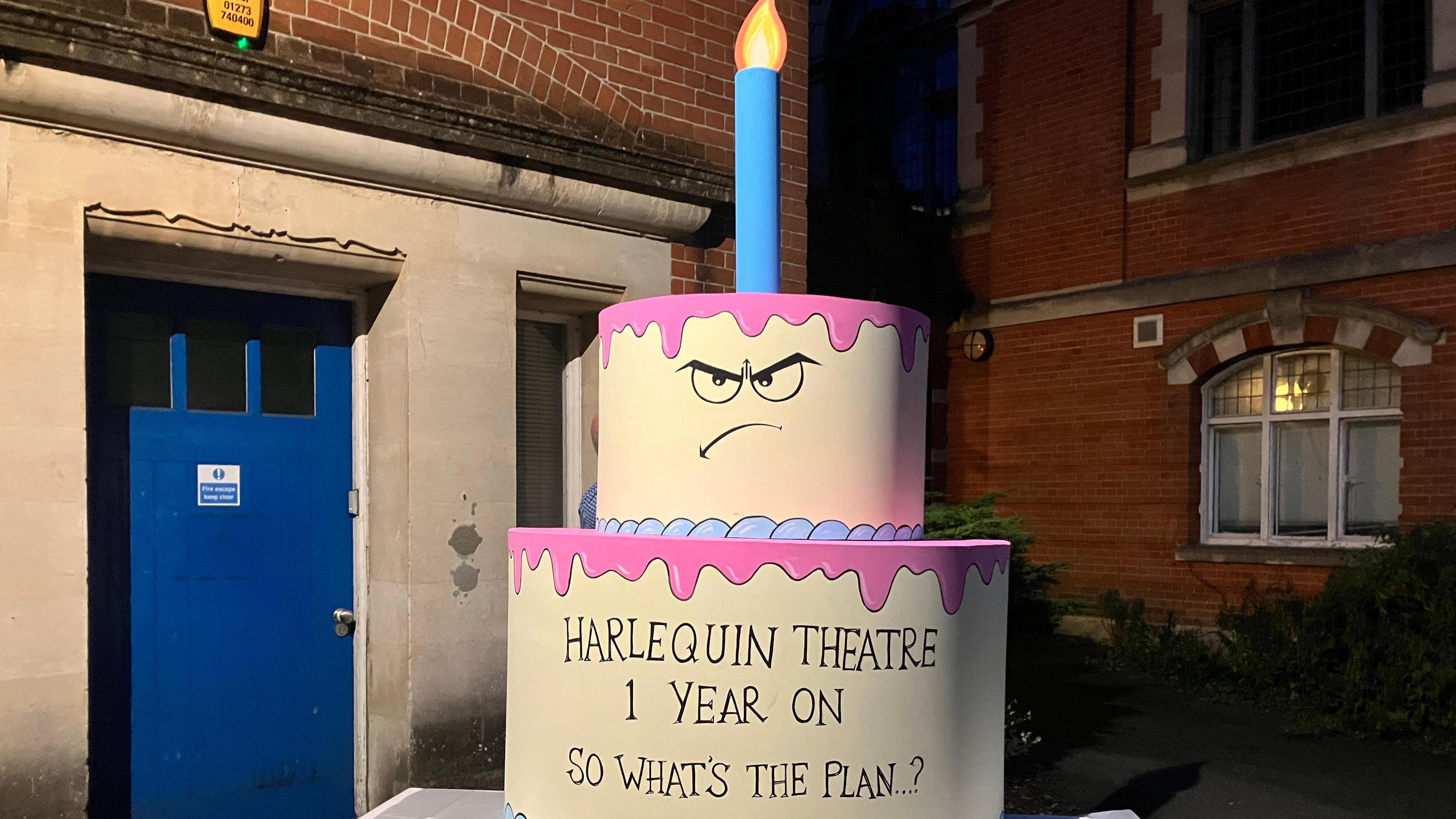 A large cake prop with the works Harlequin Theatre one year on so what's the plan...? written on it