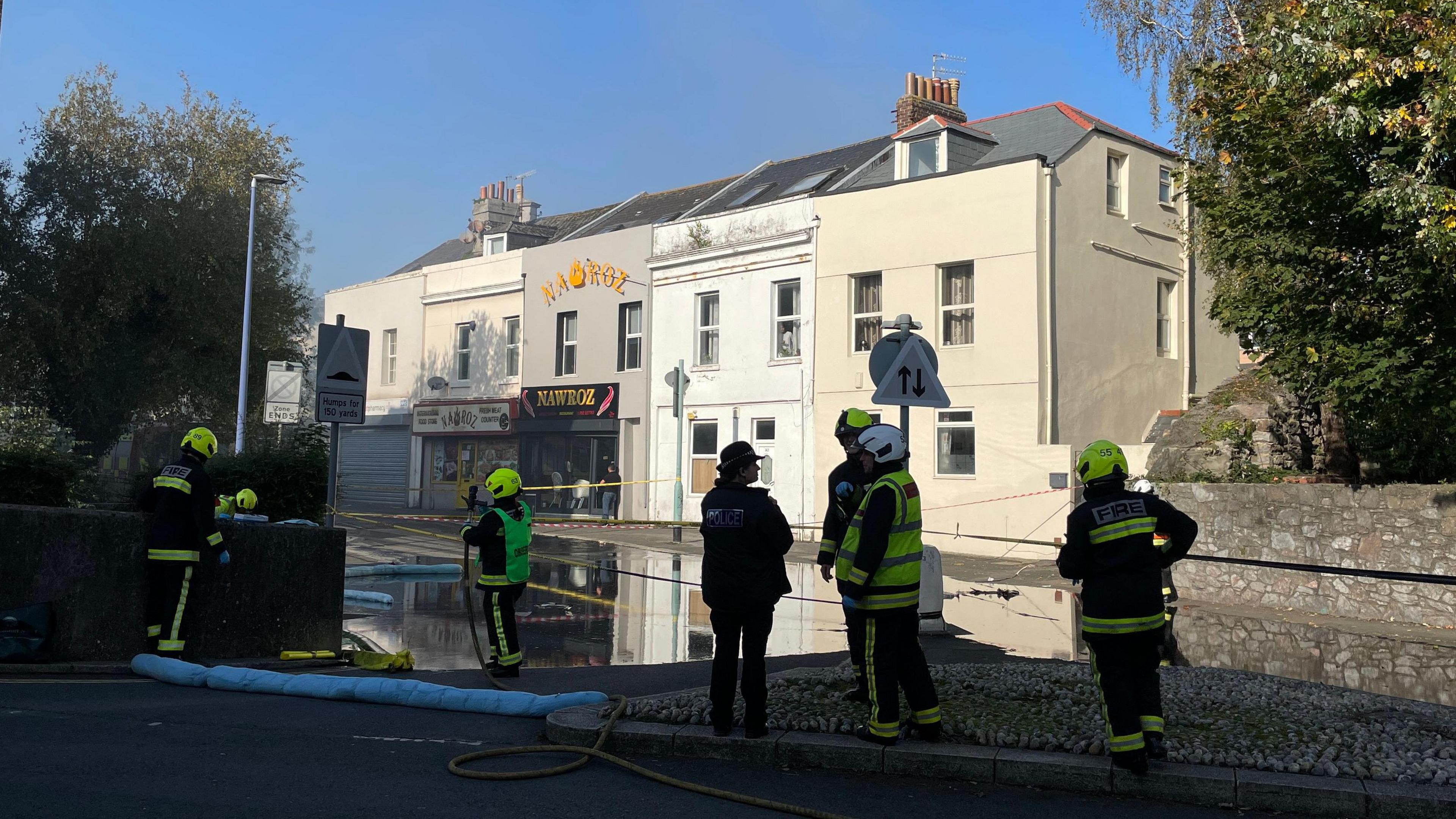 A picture of Belmont Street in Plymouth. There is firefighters on scene with smoke and a liquid substance visible.