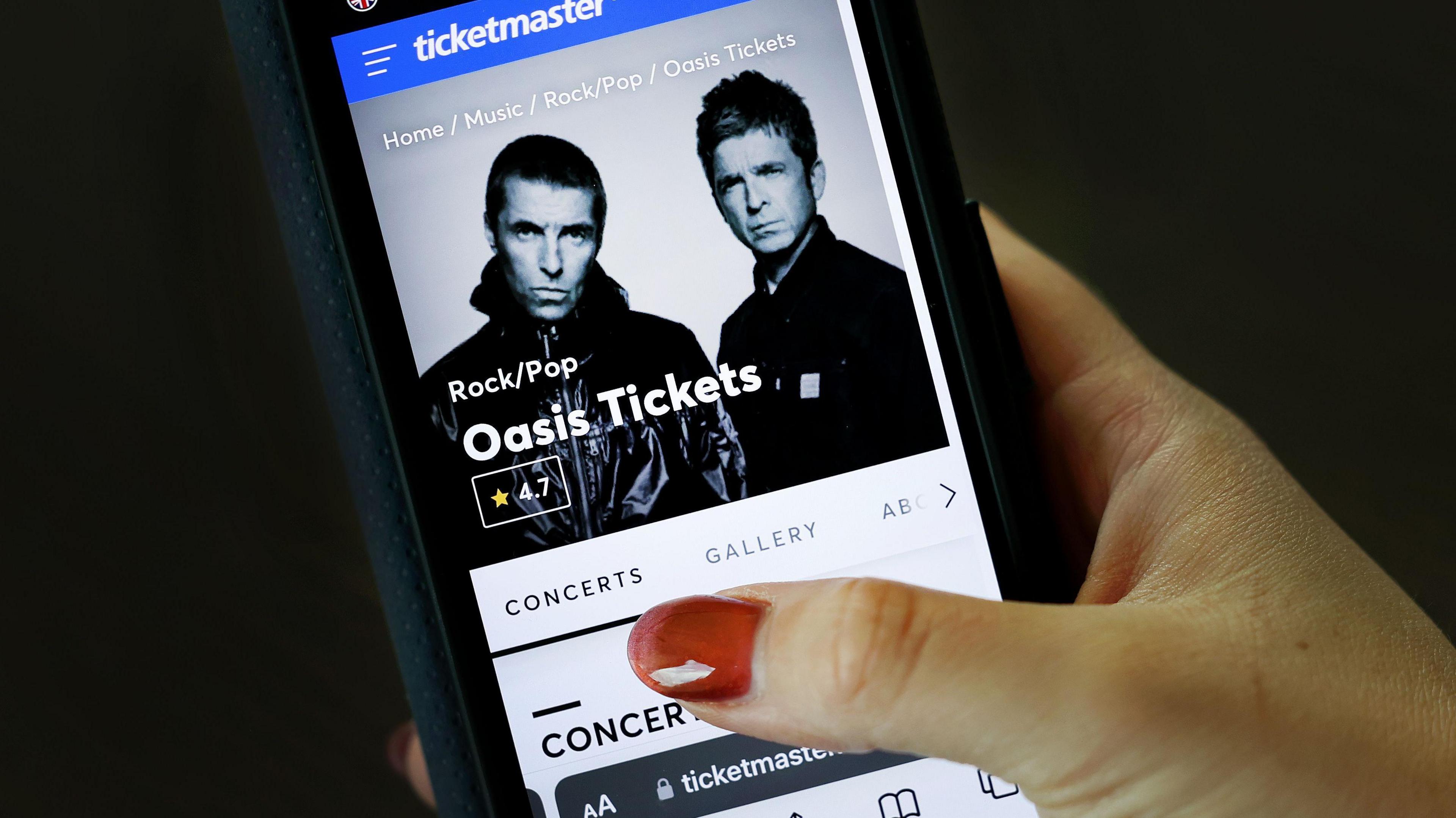 Shot of Ticketmaster website advertising Oasis Tickets on a smartphone, held in a hand with painted red fingernails