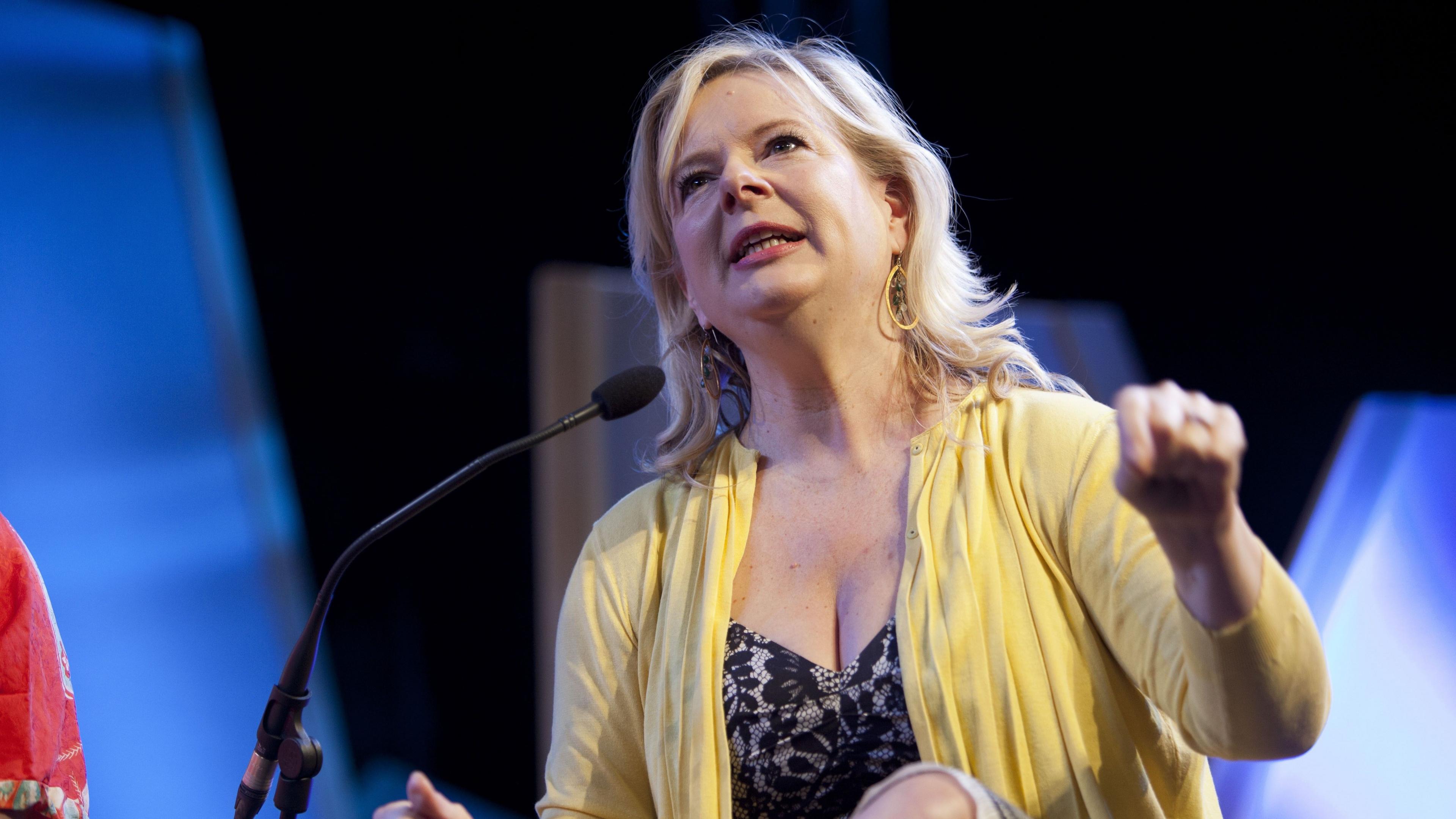 Allison Pearson is wearing a black dress and yellow cardi and is speaking into a microphone at the Hay Festival