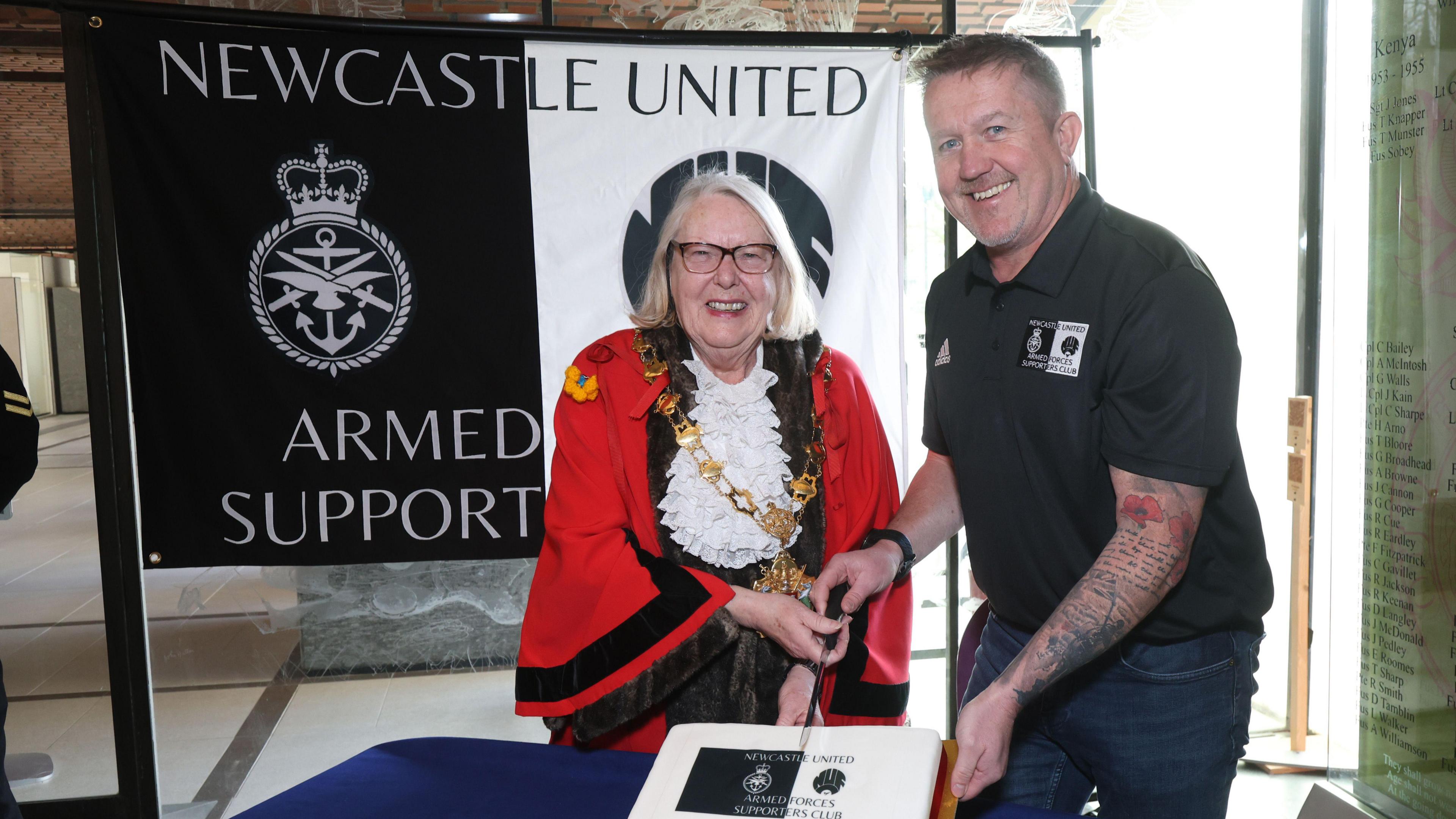 The Lord Major and Mickey Warke cutting a cake and smiling in front of the clubs banner. 