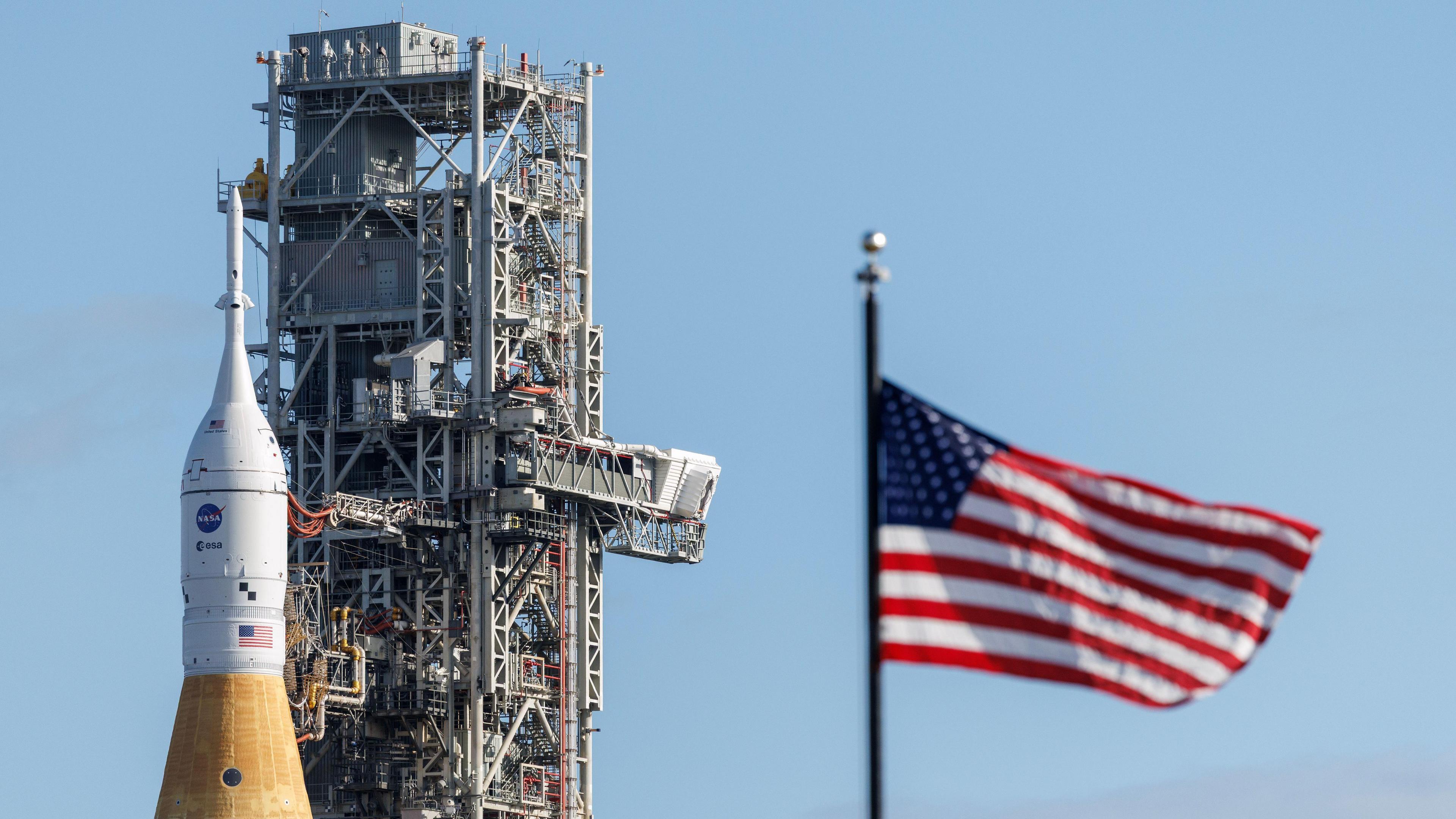 an American flag out of focus with the Artemis rocket behind it