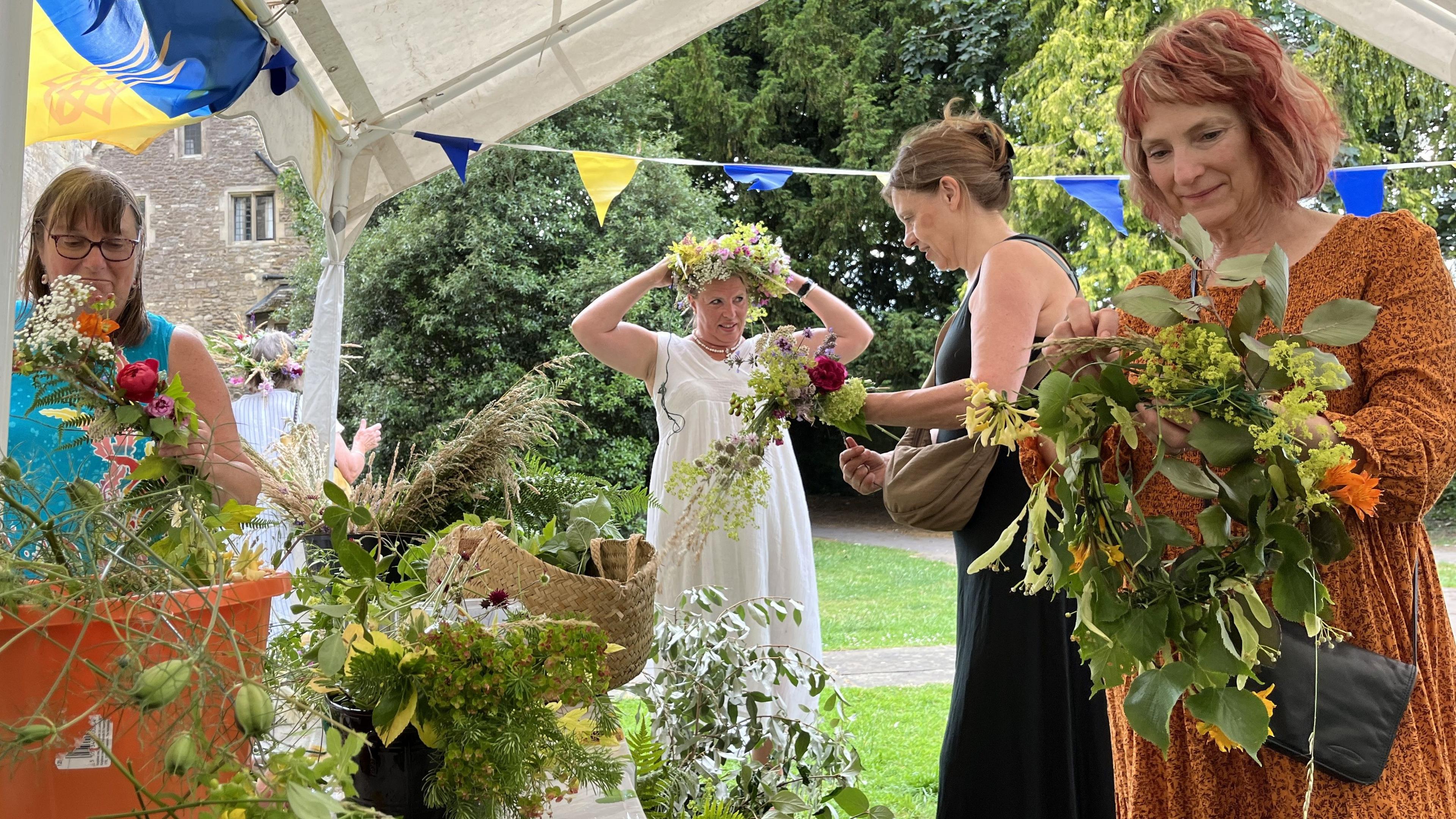 Four women making and trying on flower crowns.