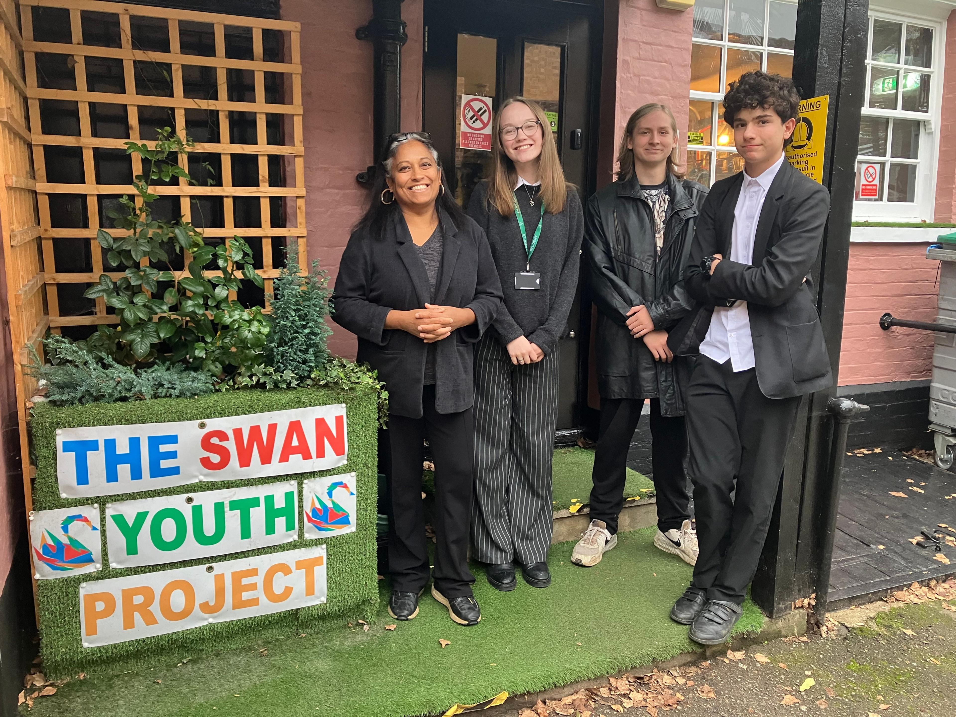 A picture of a middle aged woman wearing black, a teenage girl and two teenage boys, who are also all wearing black, outside The Swan Youth Project in Berkhamsted.