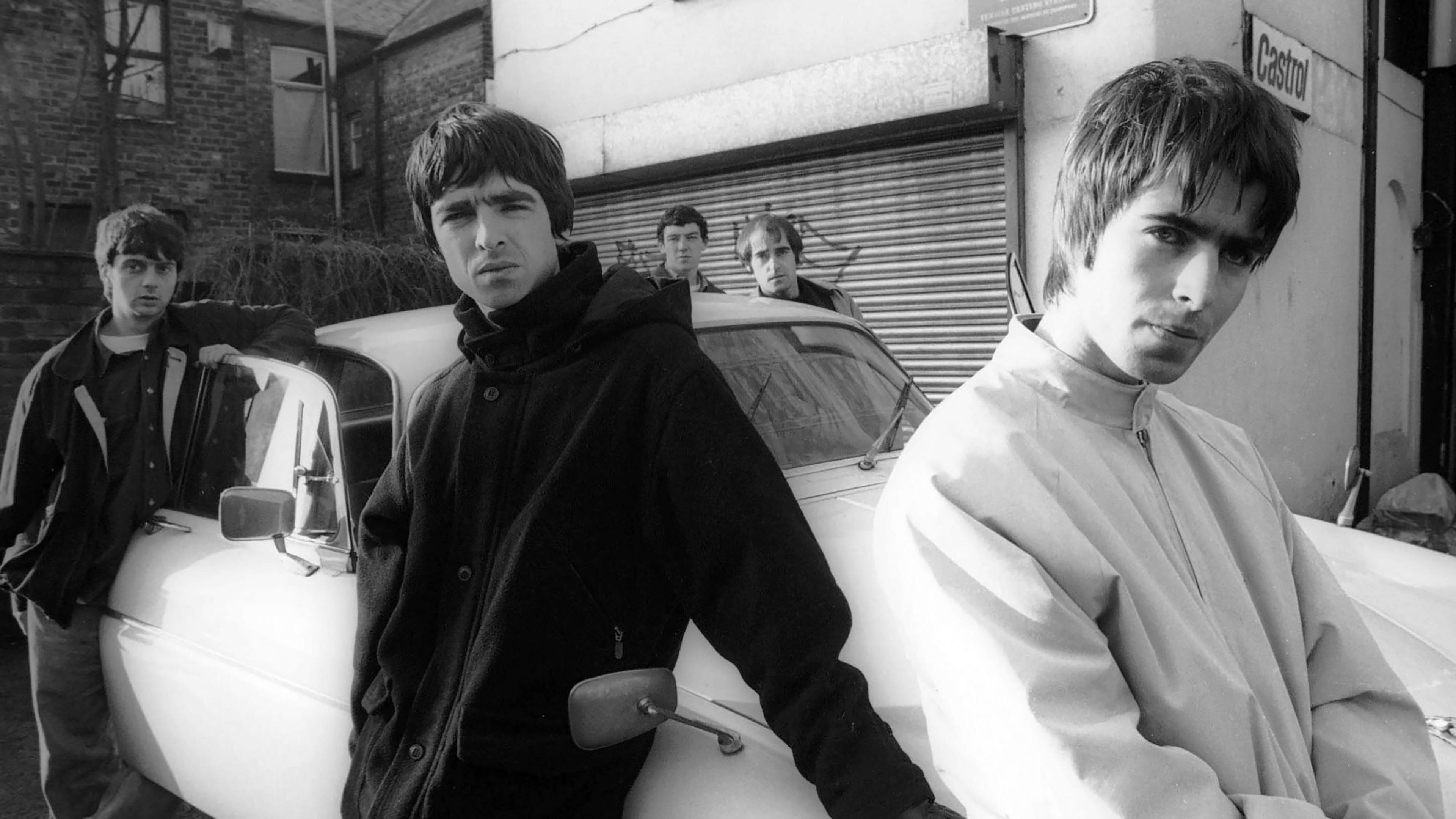 Group portrait of British rock band Oasis leaning against a Jaguar XJ6 car in Withington, Manchester taken by James Fry on 30 November 1993