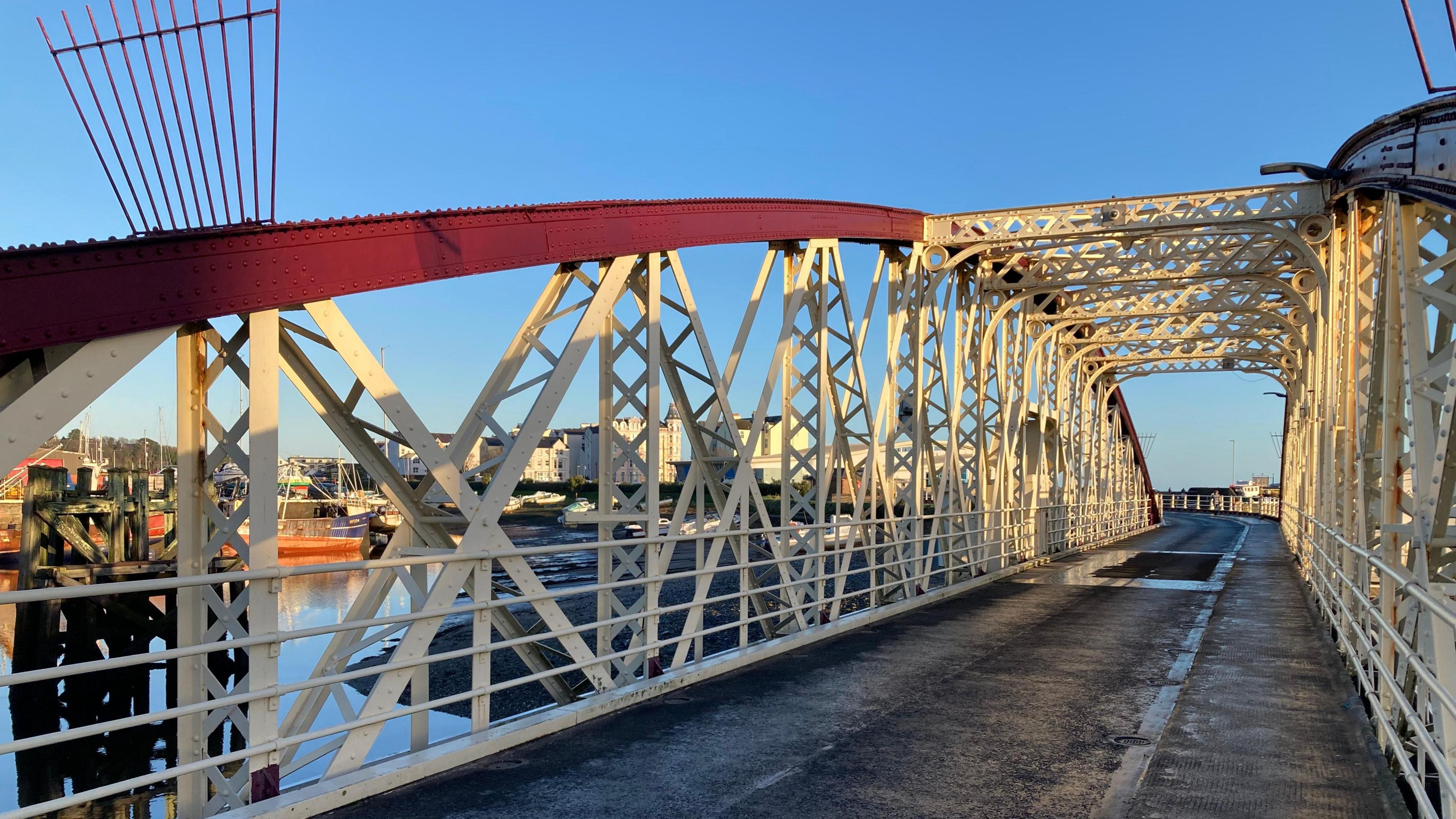 The view of the bridge road which has a red arching structure with white metal bars.