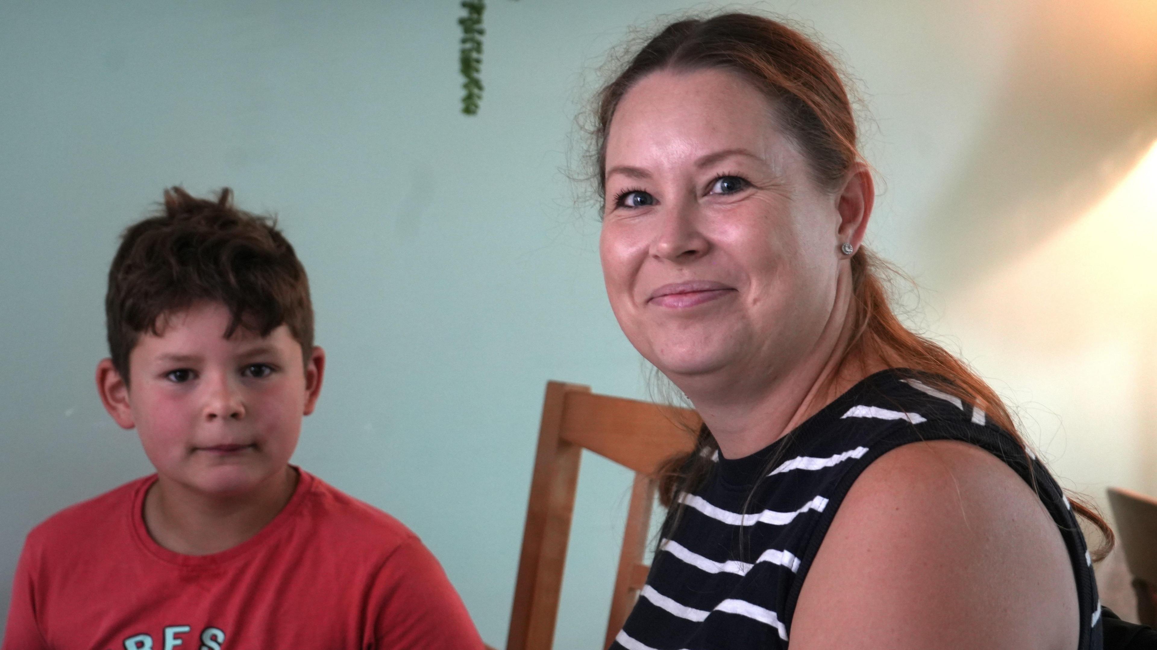 A little boy in a red T-shirt and his mother, in a black sleeveless top with white stripes, look directly at the camera.
