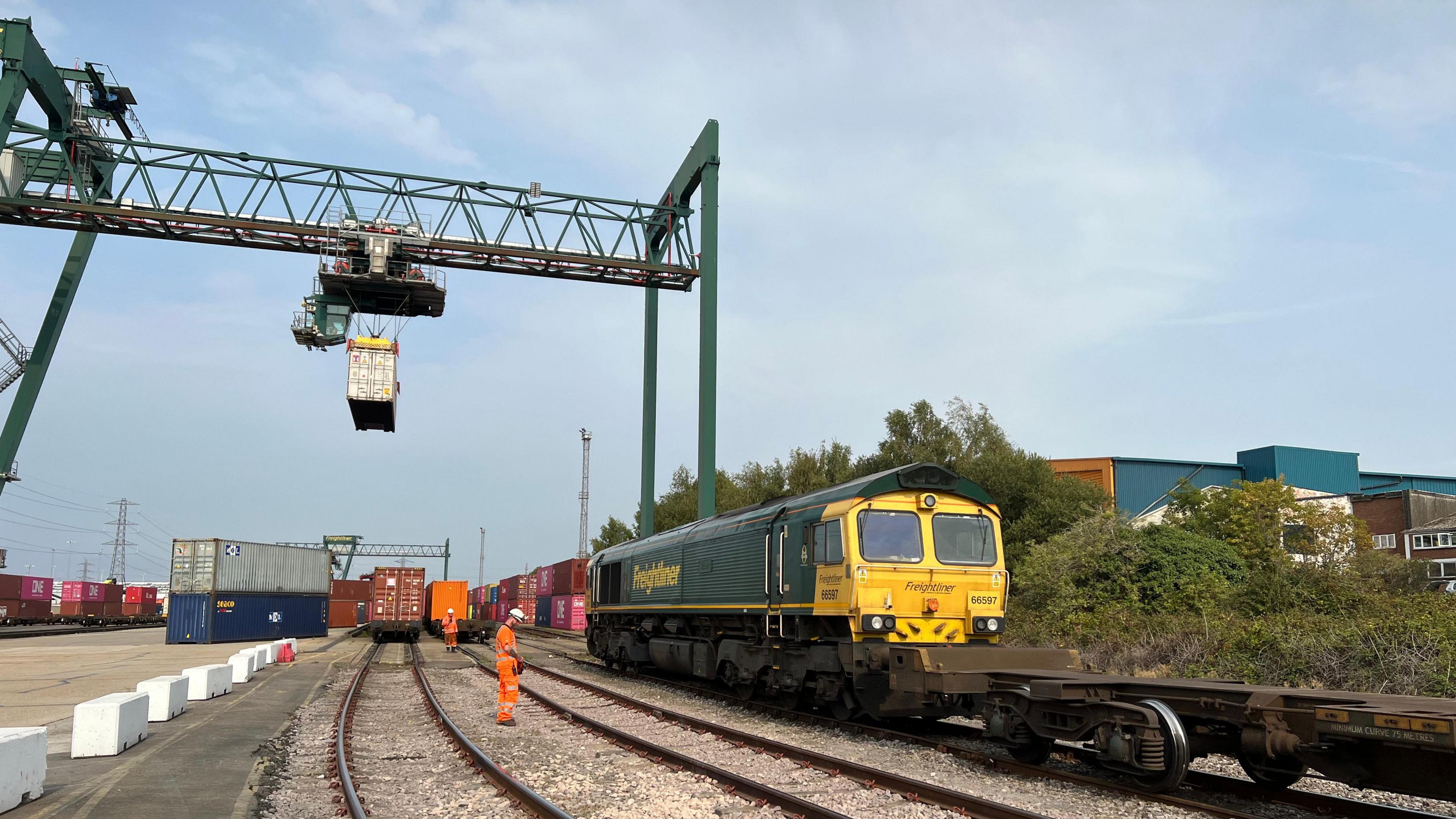 An overhead crane lifts a container onto a train while another waits to be loaded.