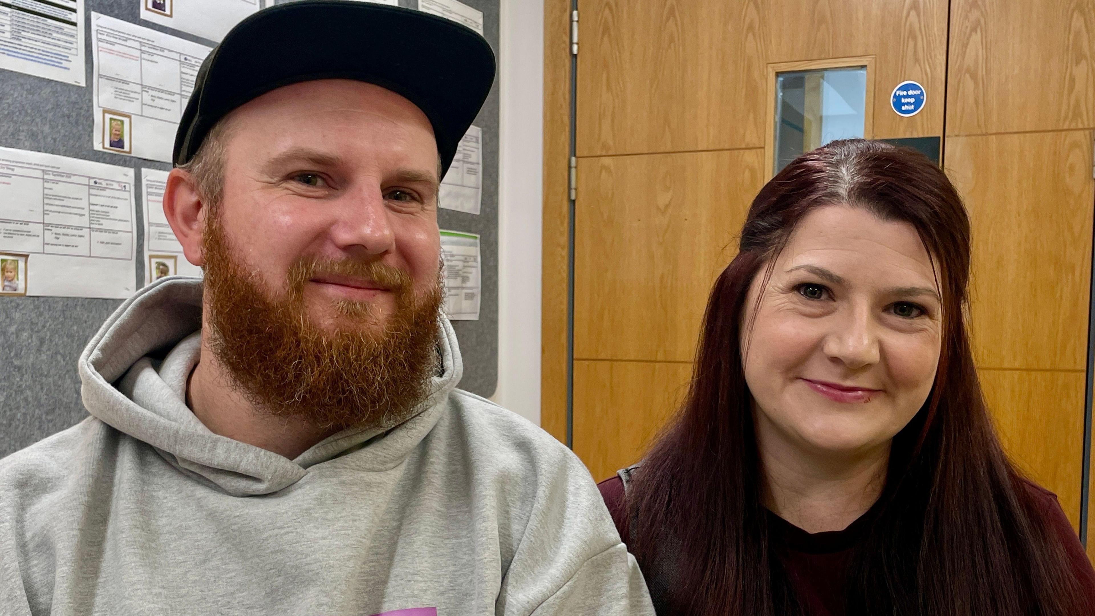 Parents Adam and Abbie Holliman smile at the camera sitting side by side.
