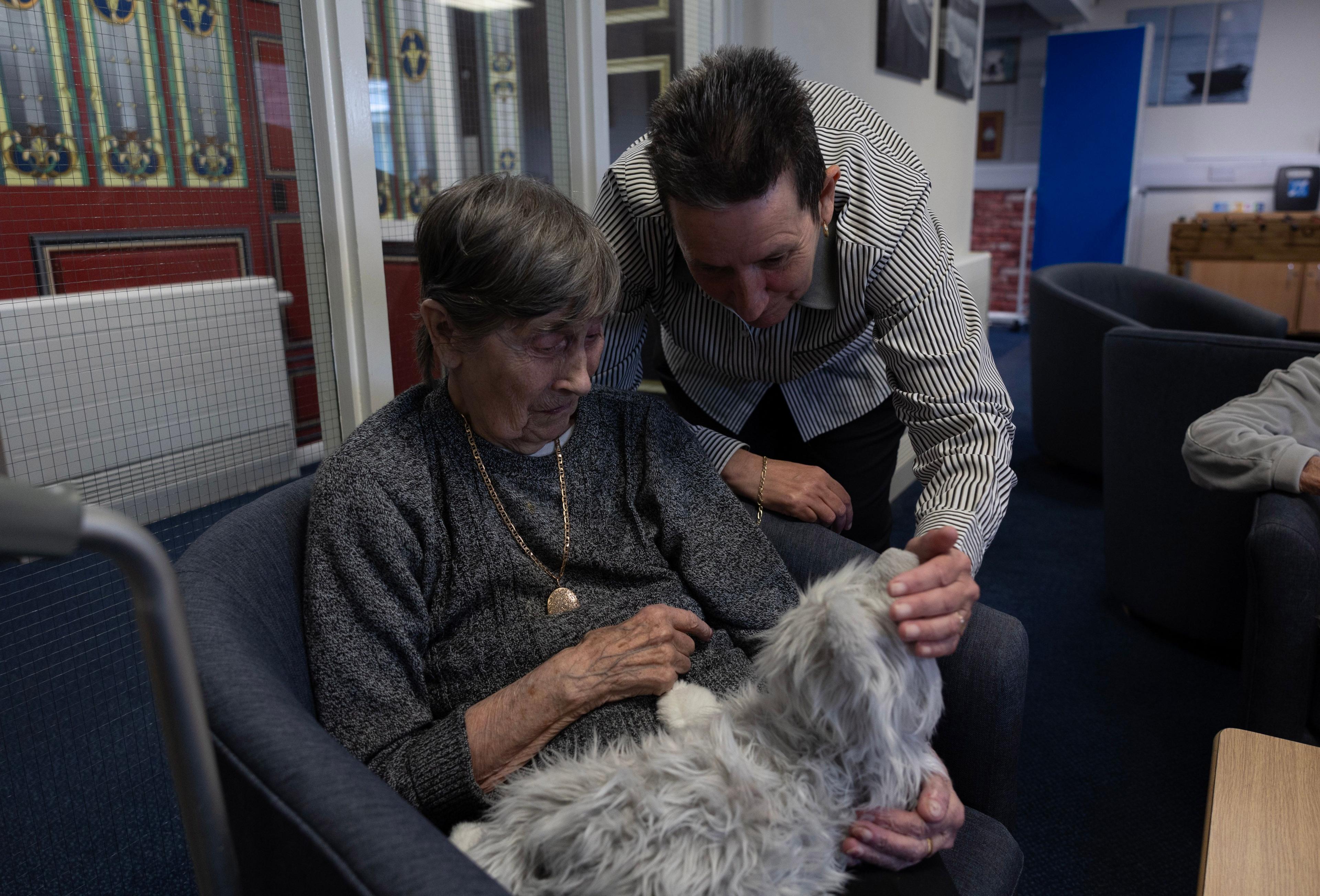 Female care home resident holds toy dog (left) while a man (right) pets a toy dog held