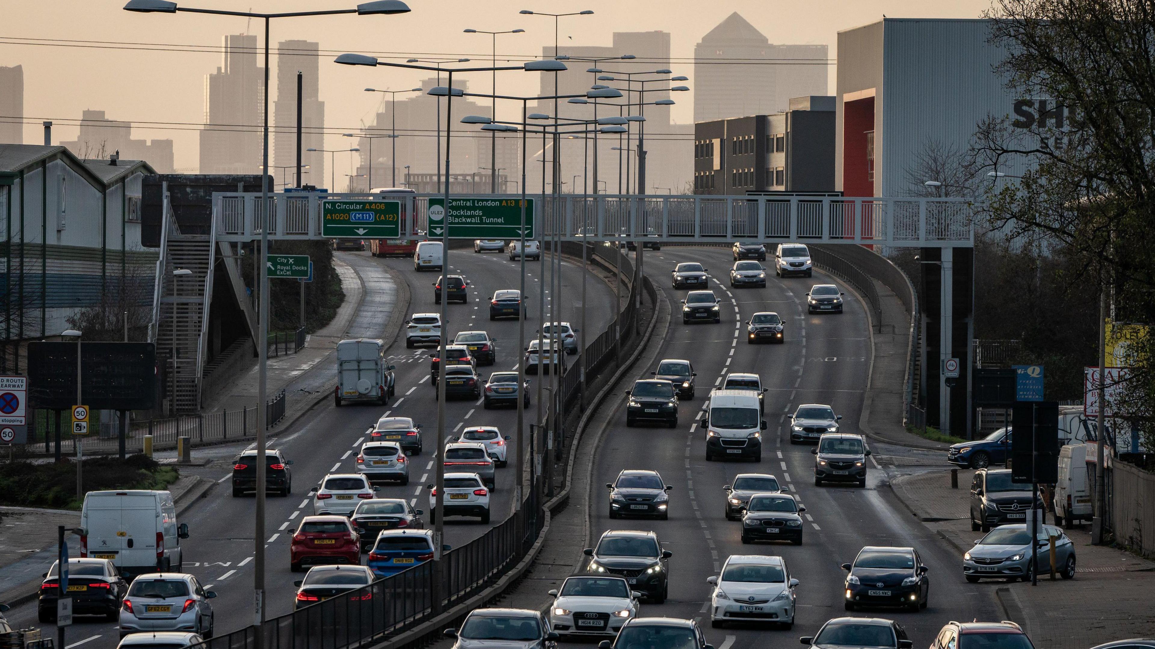 A busy road with three lanes of traffic in each direction and London's Docklands in the background