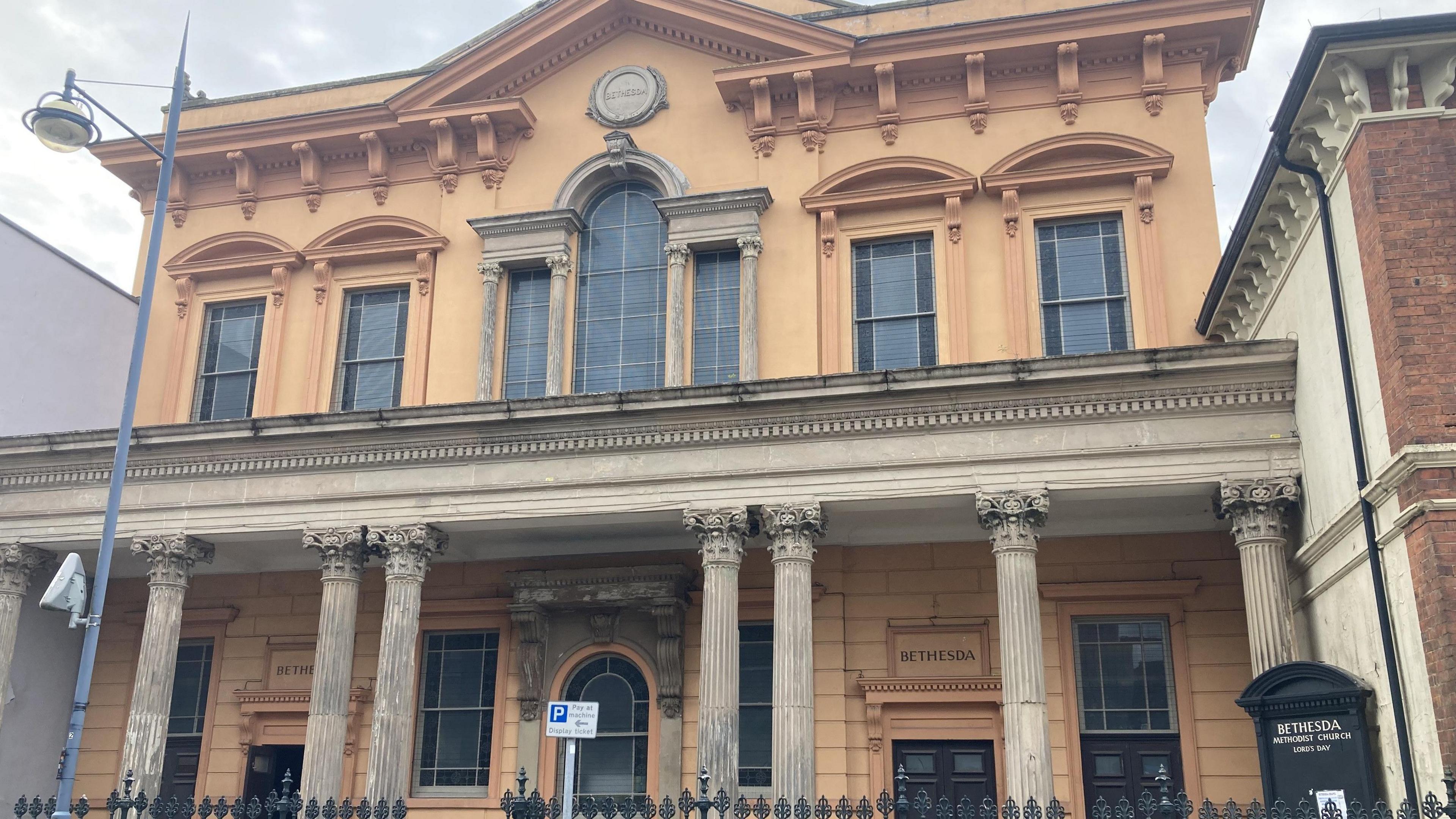 A two storey, peach-coloured church building with old-fashioned pillars in front of it.