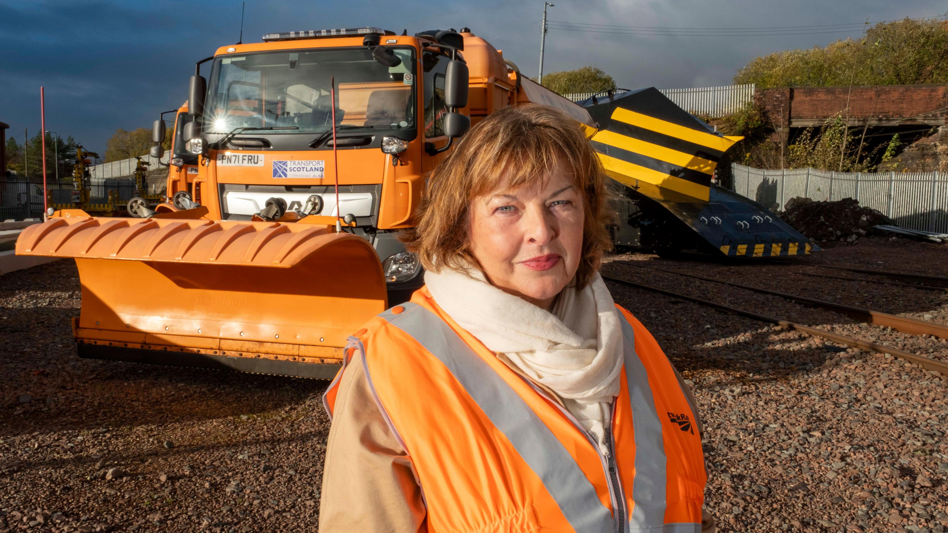 Fiona Hyslop standing in front of a snow plough with an orange hi-viz vest.