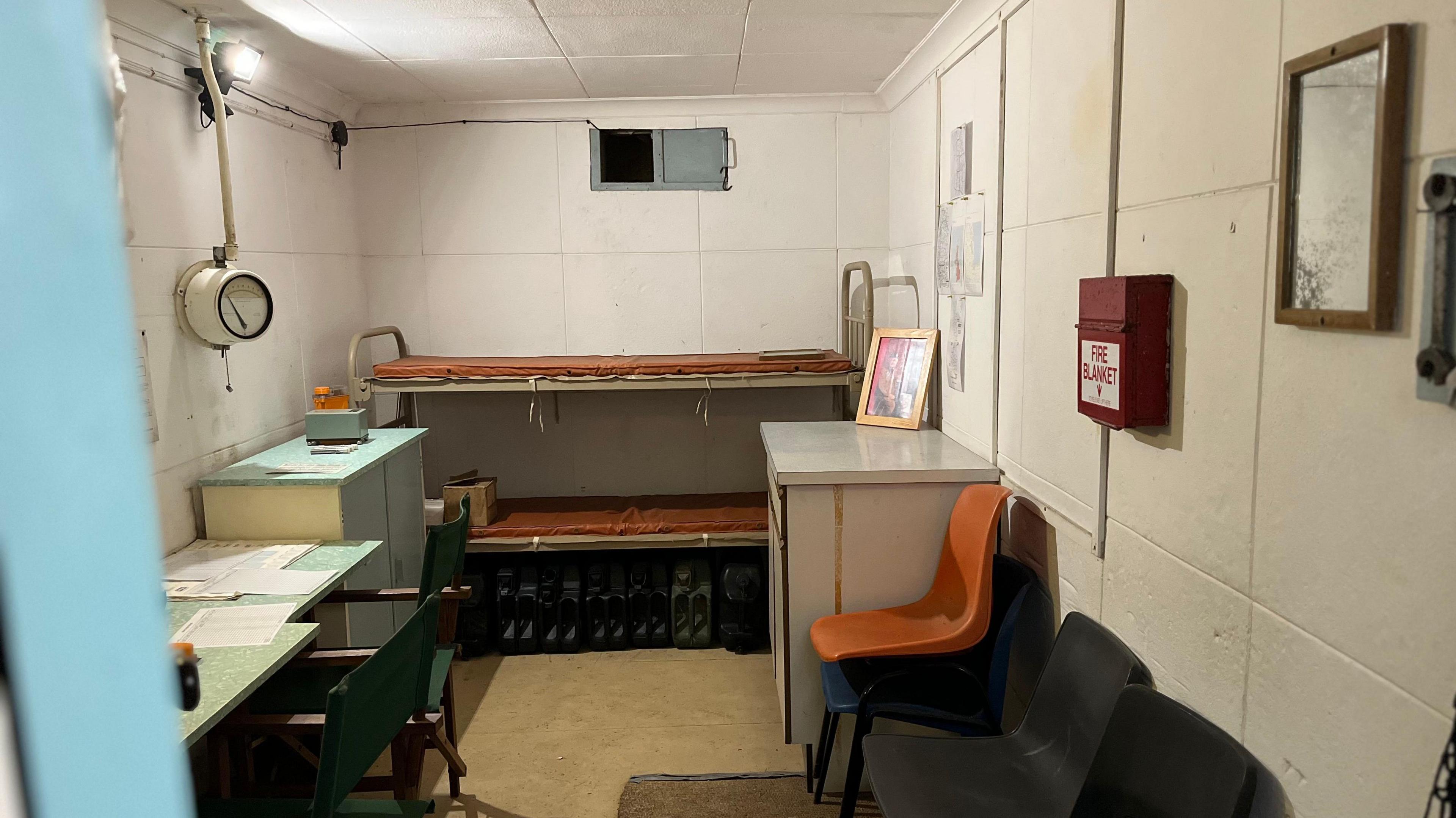 An underground bunker with bunk beds, a chair, desk and equipment 