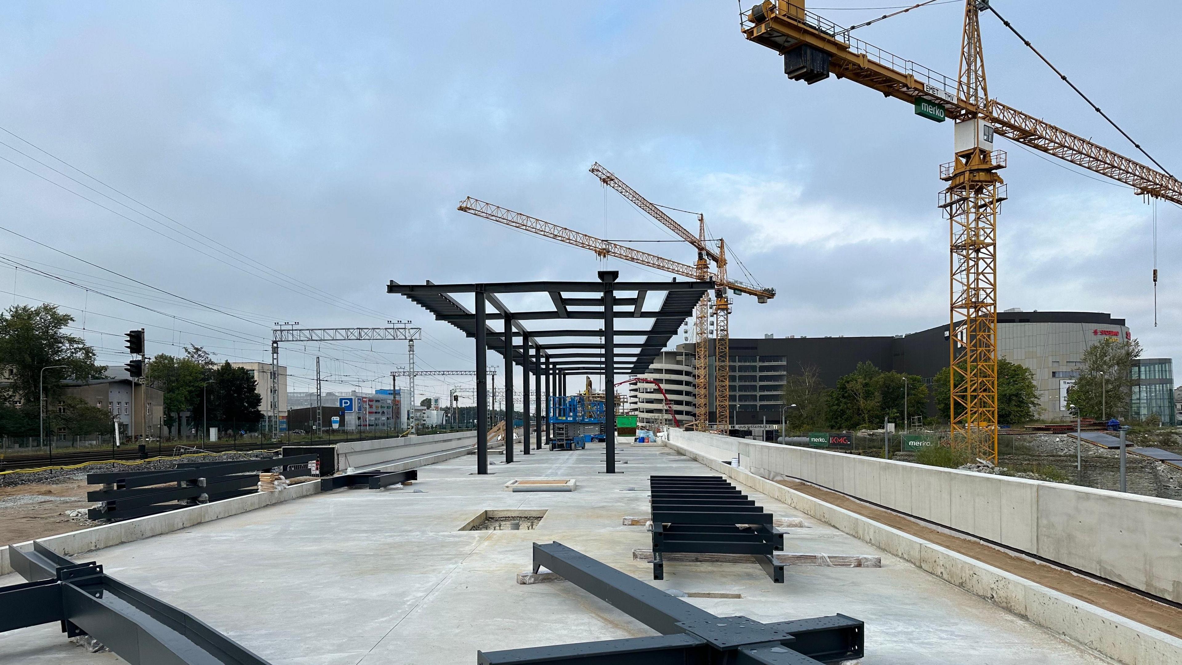 An unfinished platform stretches ahead, with black slats lying on the concrete and rising in a half-constructed structure, beside a crane