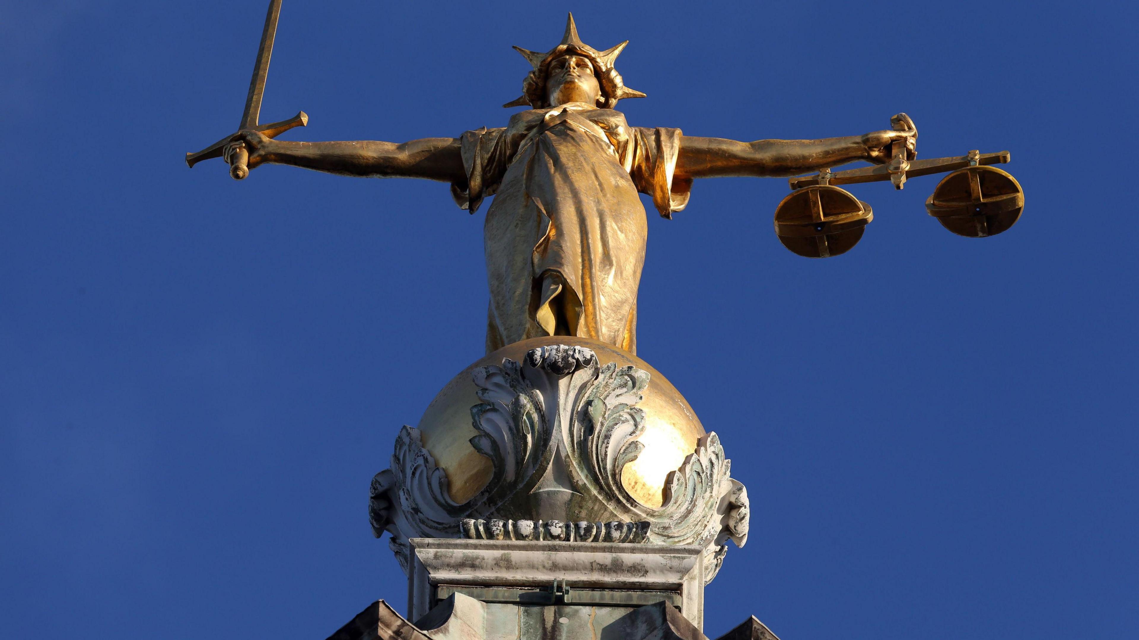 A statue representing justice, holding a sword in one hand and scales in the other, standing above the Old Bailey in London