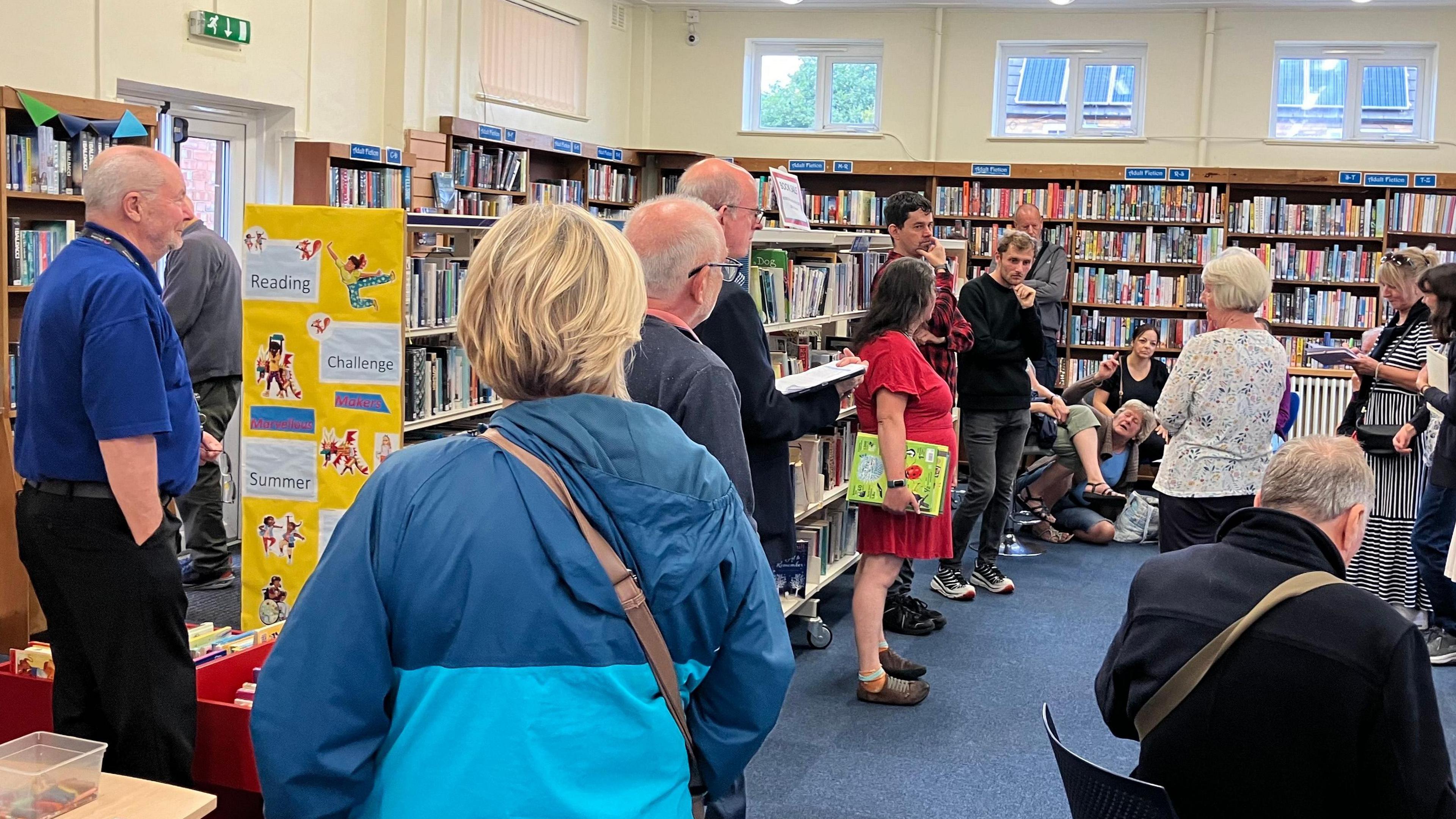 People standing and talking in the library surrounded by bookshelves full of books