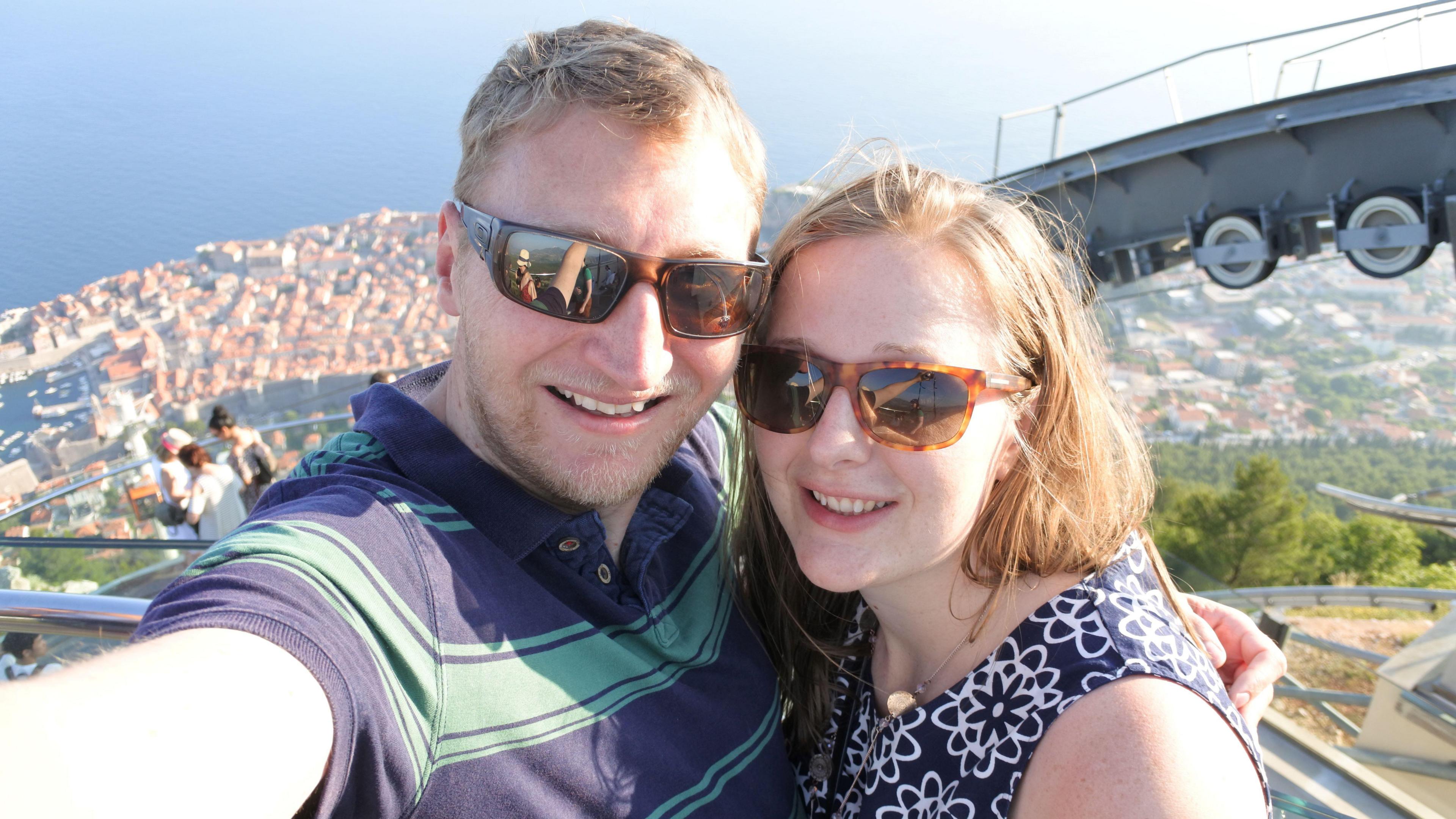 Jamie and Kate Scott pictured in a selfie while on holiday. They both wear sunglasses and the shot shows them up high with a view of seaside town behind them below.